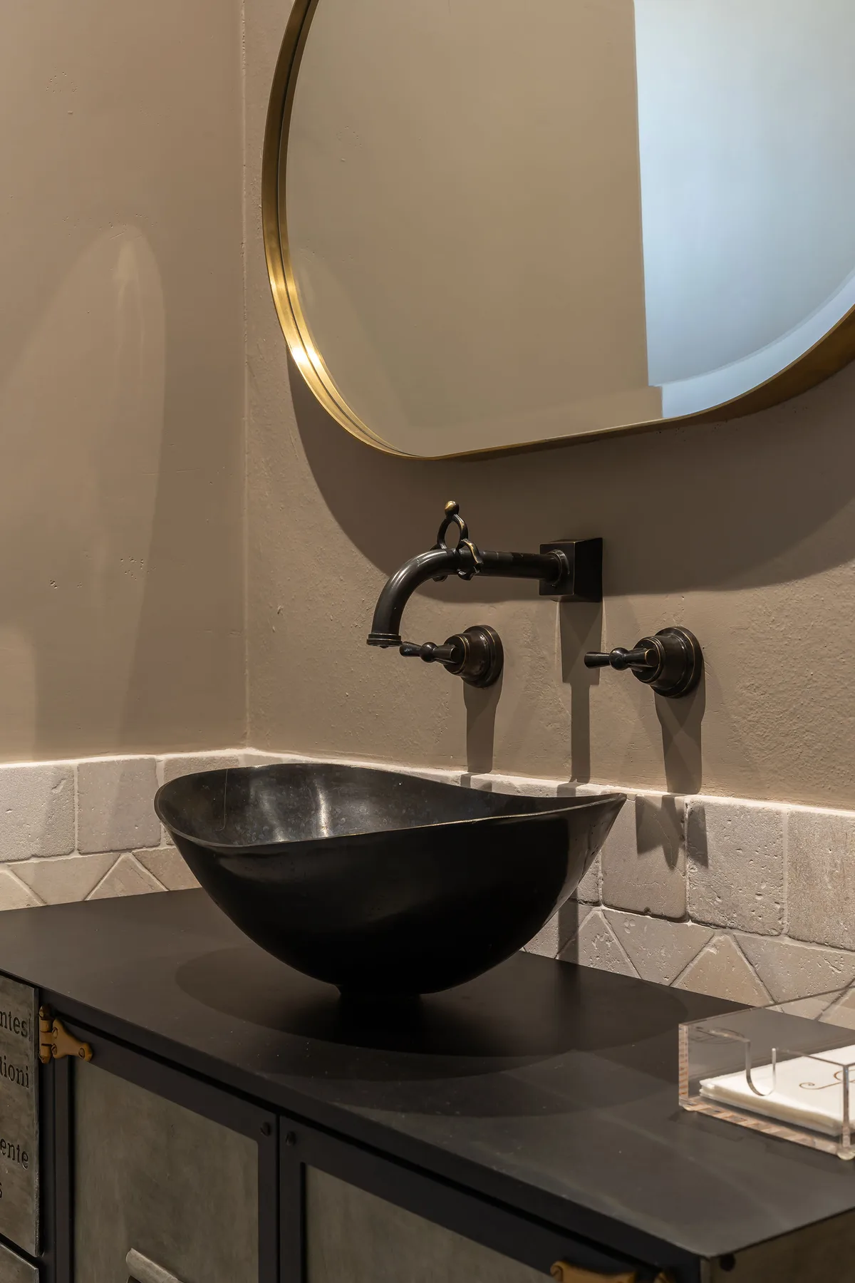 A bathroom vanity with a dark vessel sink beneath a rounded mirror.