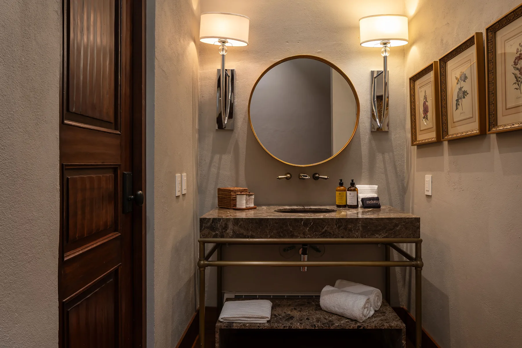 A bathroom vanity with a round mirror, wall lights, and framed artwork.