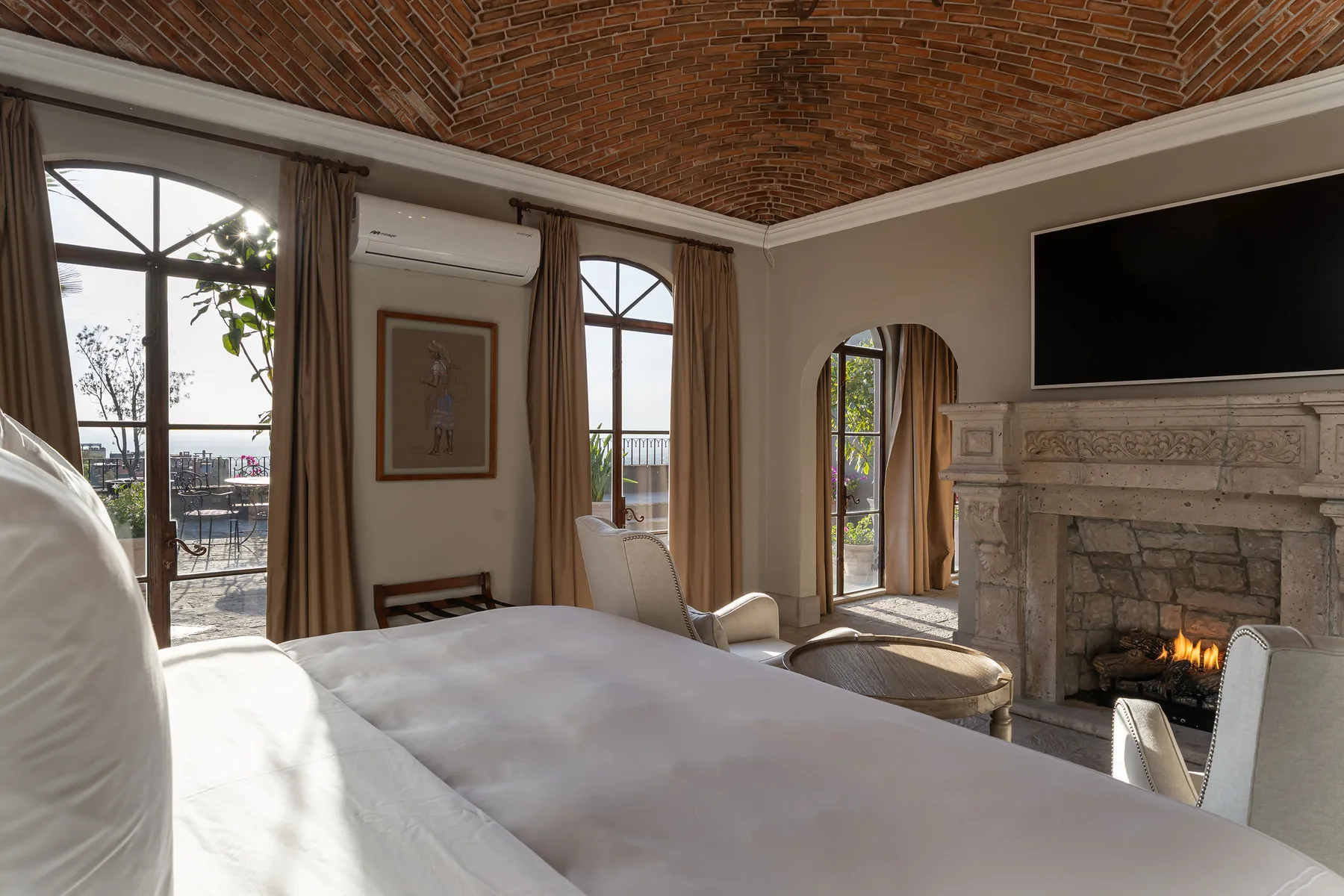 A bedroom with a large bed, arched windows, and a fireplace.