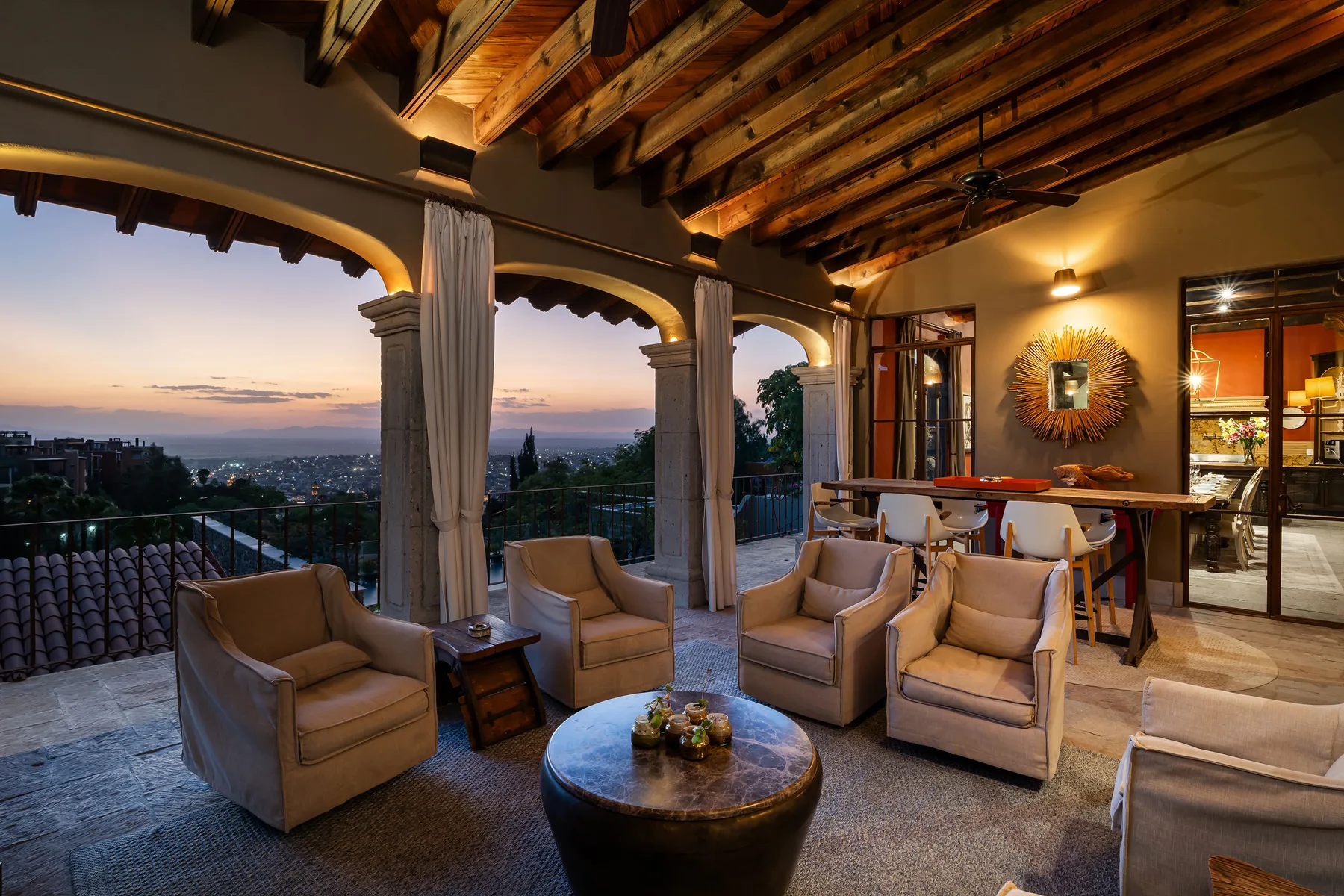 A covered outdoor seating area overlooks a city at sunset.