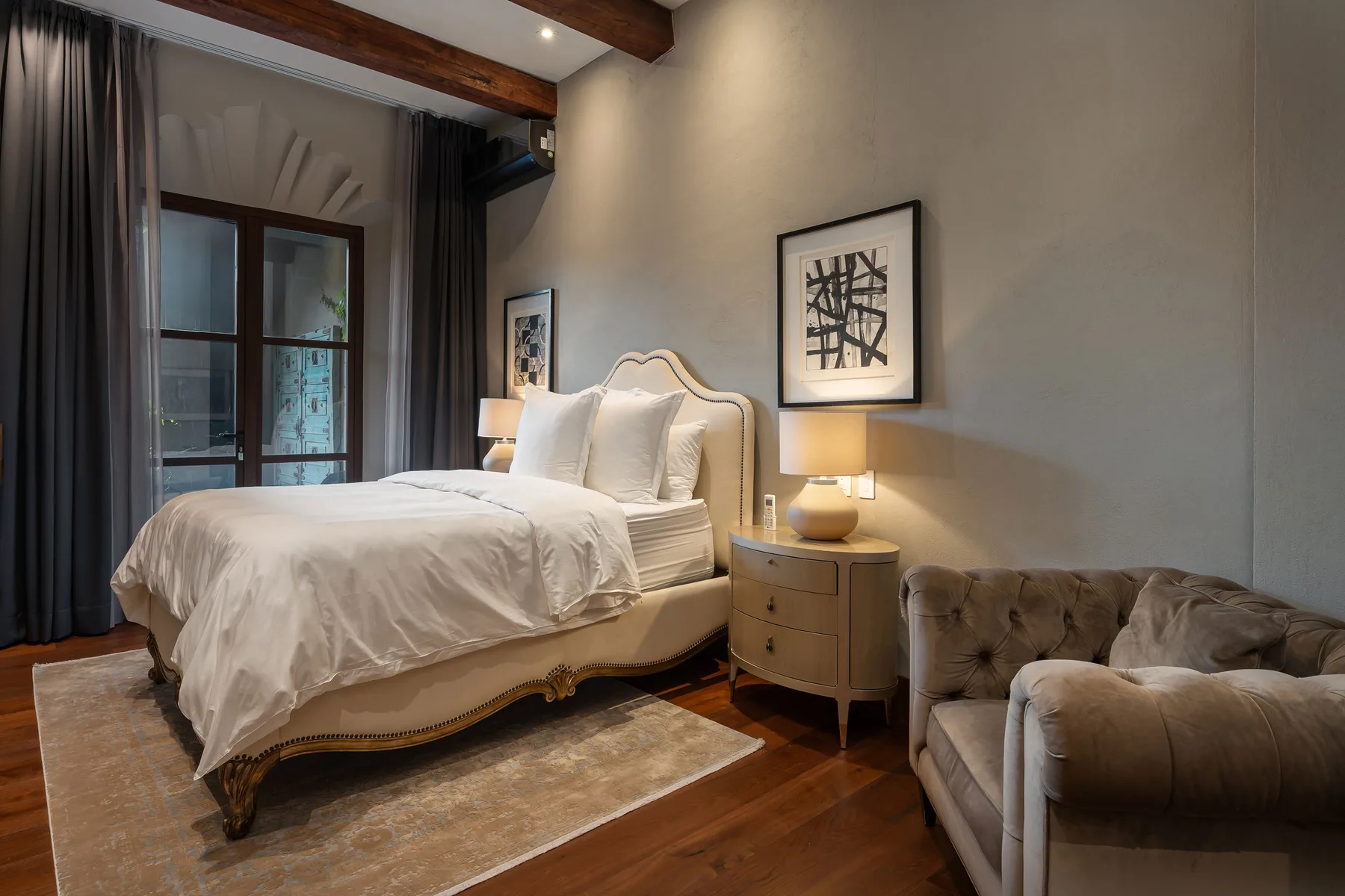 A bedroom with a neatly made bed, bedside table, and upholstered seating.