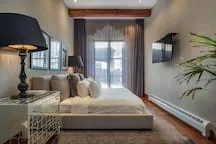 A bedroom with a bed beside windows and a wall-mounted television.