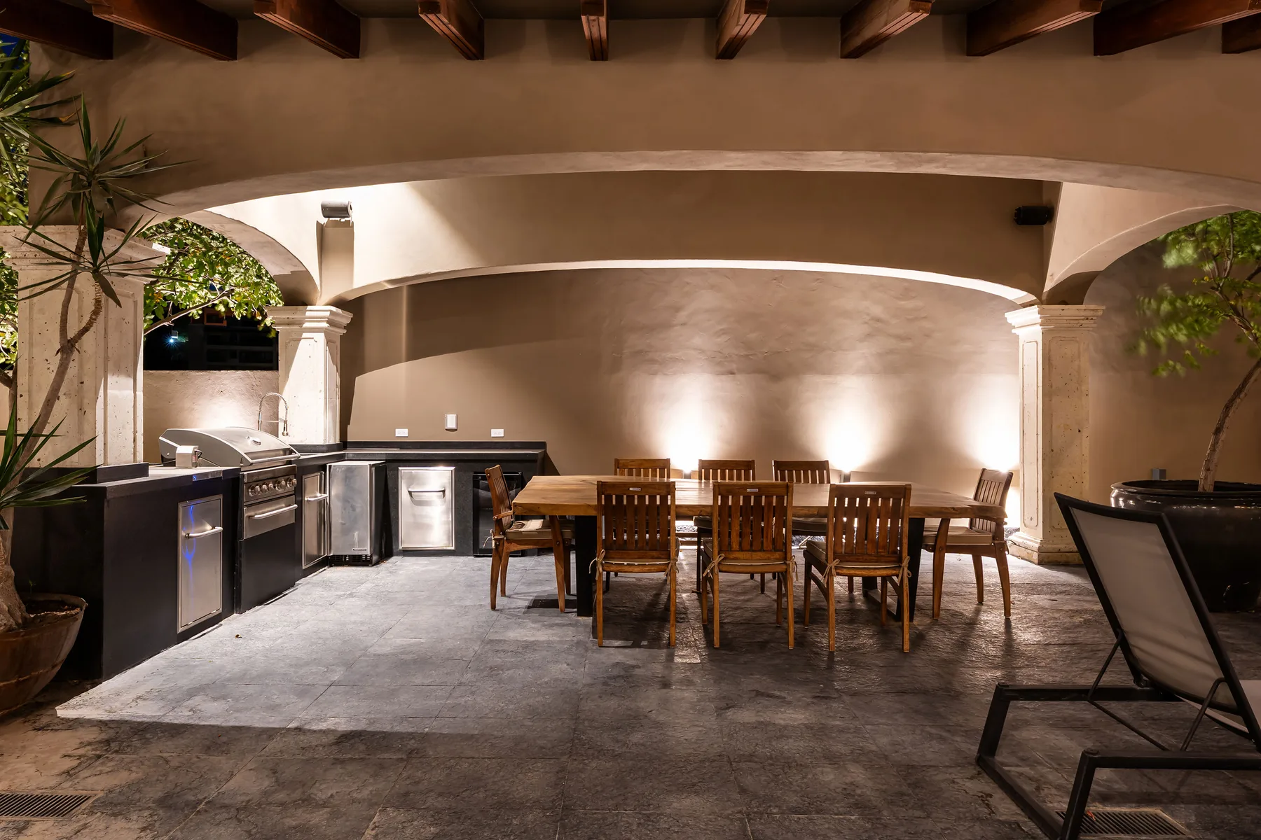 A covered outdoor dining area with a long wooden table and kitchen counter.