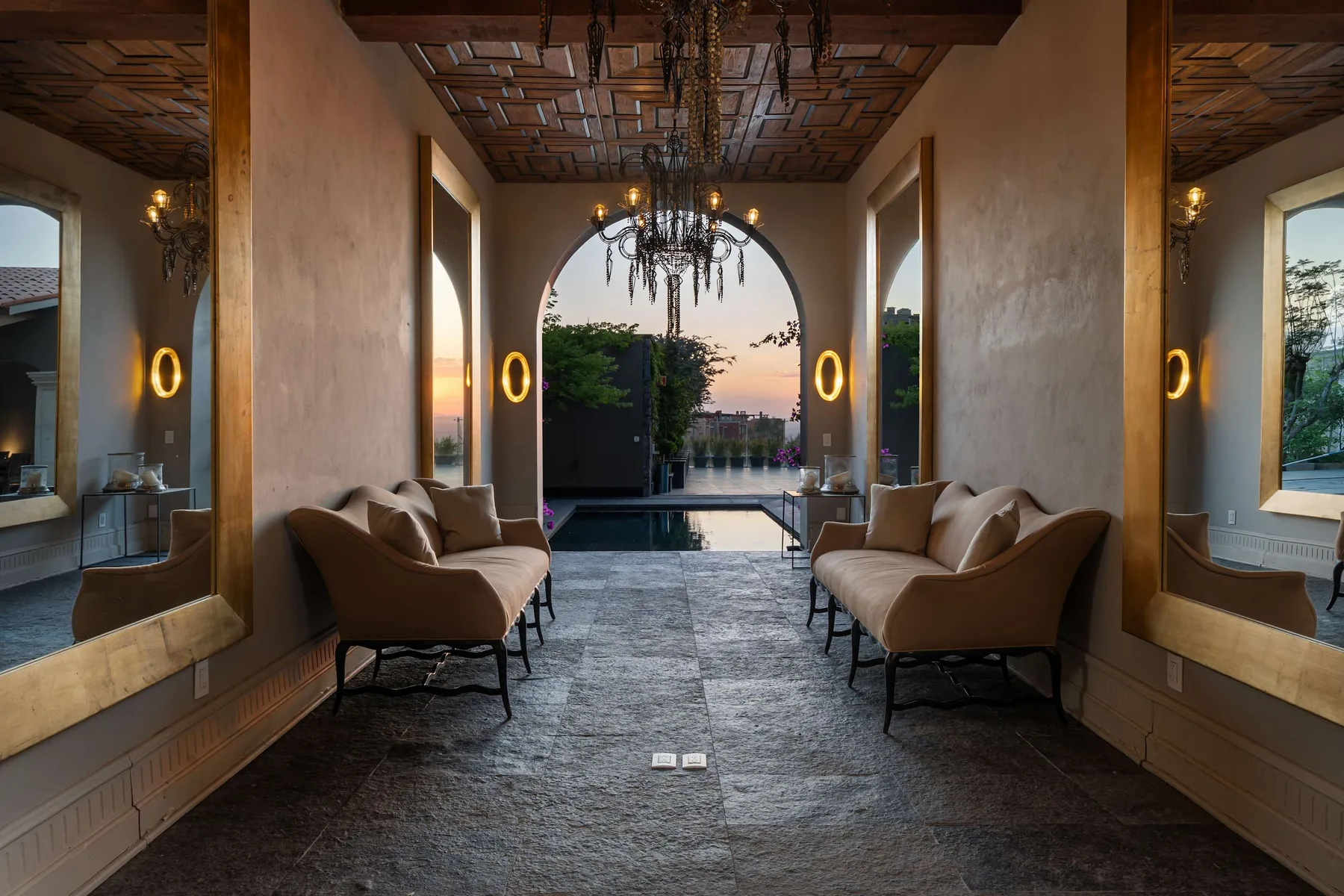 An elegant lounge with seating faces an arched opening and a pool.