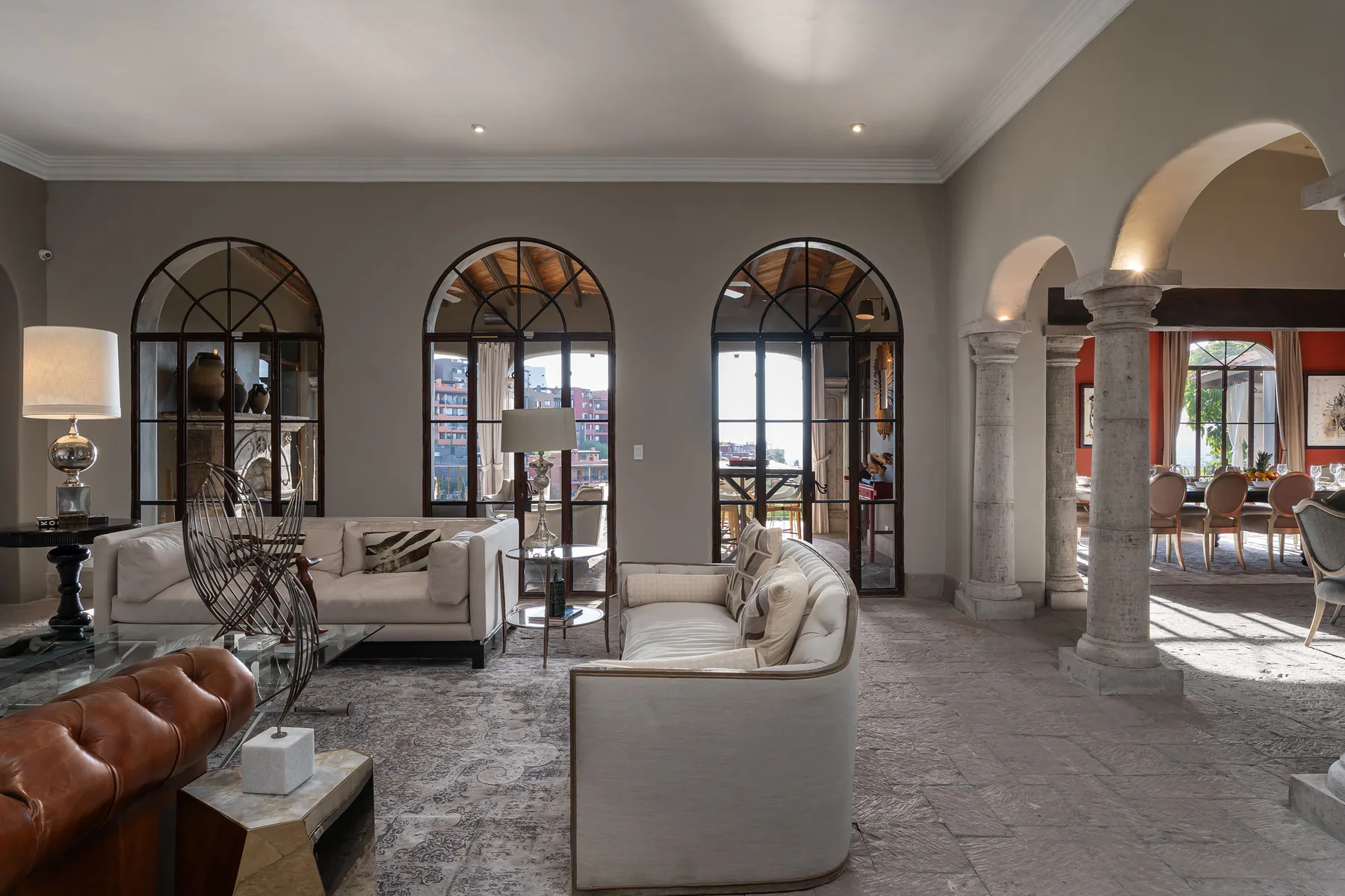 A spacious living room with seating, arched windows, and stone columns.