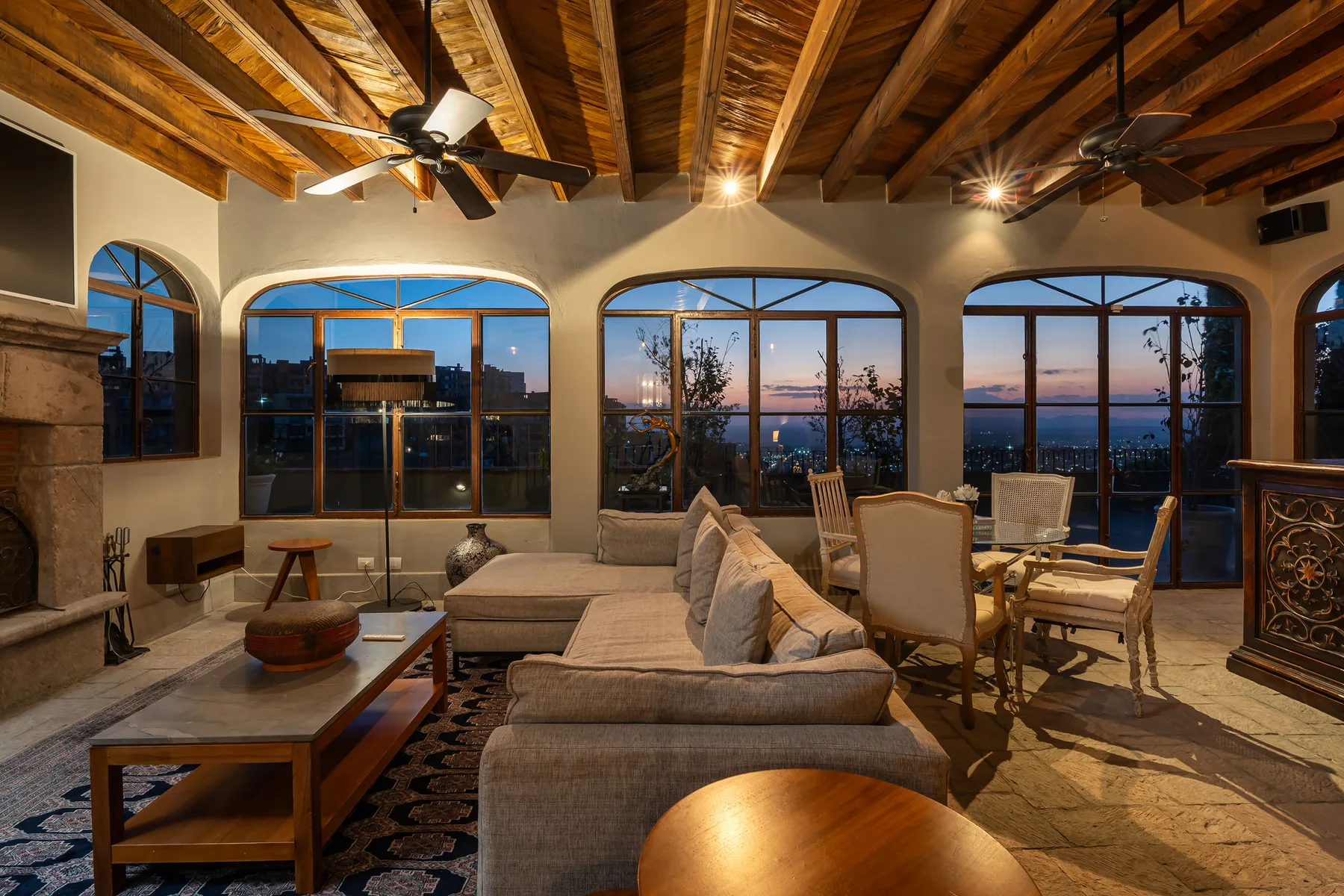A living room with seating and large arched windows overlooking the water at dusk.
