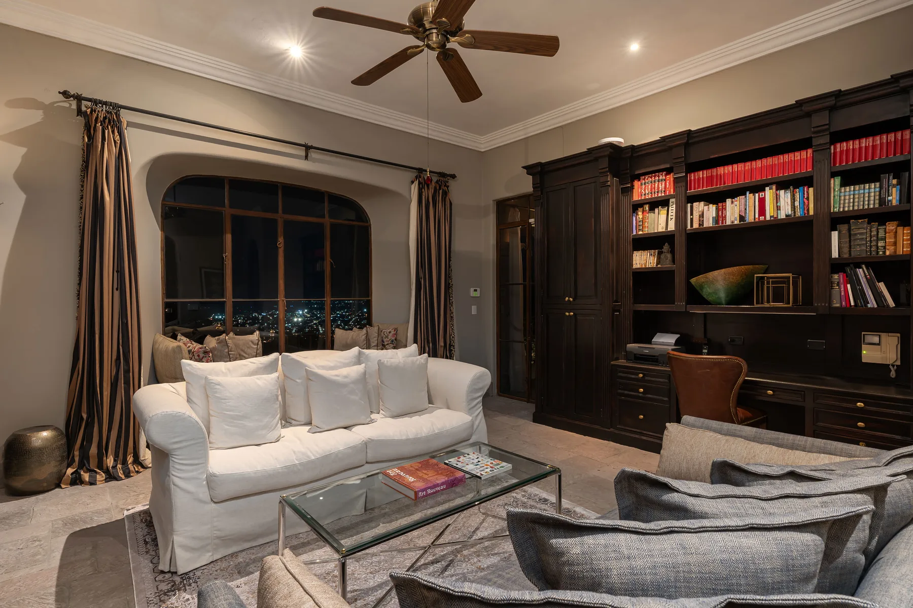A living room with a white sofa, glass coffee table, and dark built-in bookshelves.