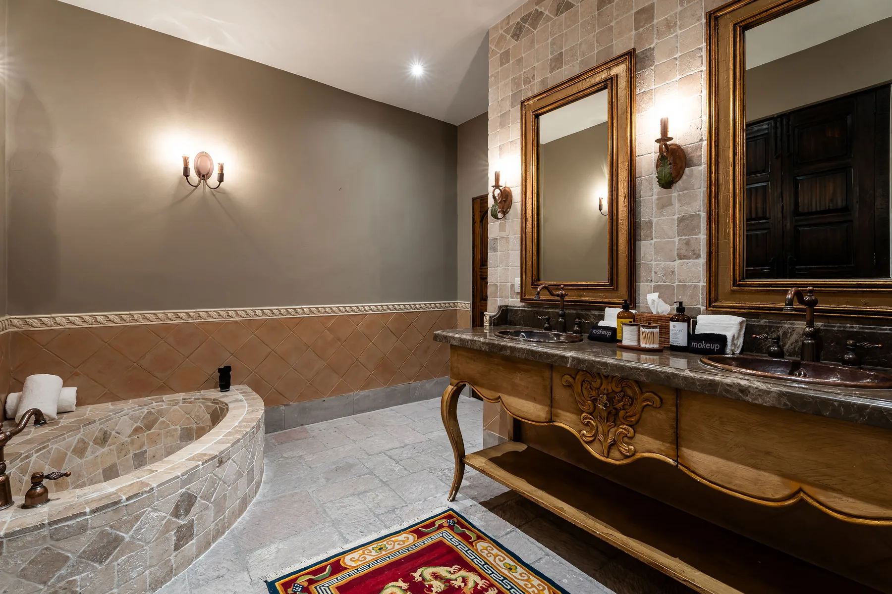 A bathroom with a curved tiled bathtub and an ornate wooden vanity.