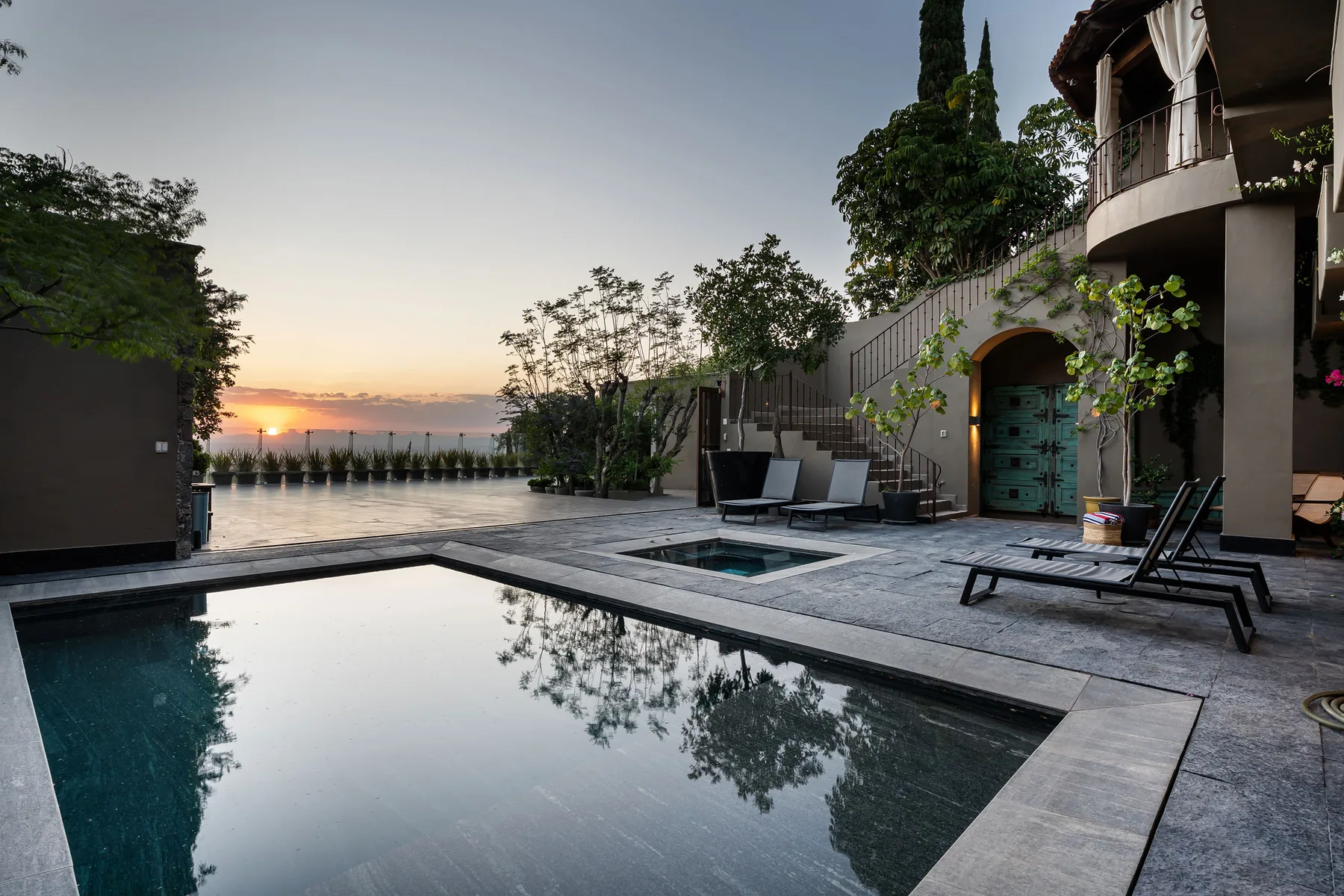 A courtyard pool beside a modern building, with outdoor seating at sunset.