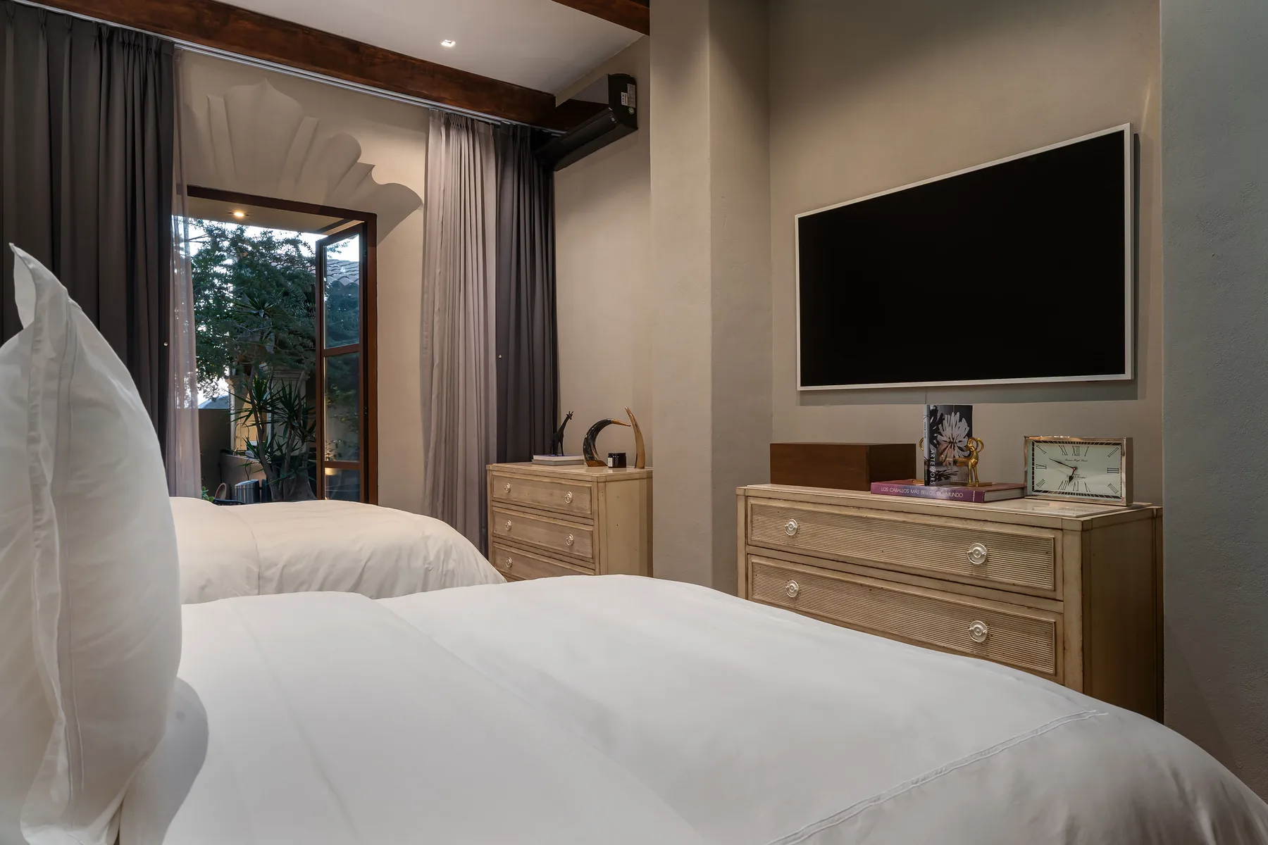 A bedroom with white beds, a television, and a curtained glass door.