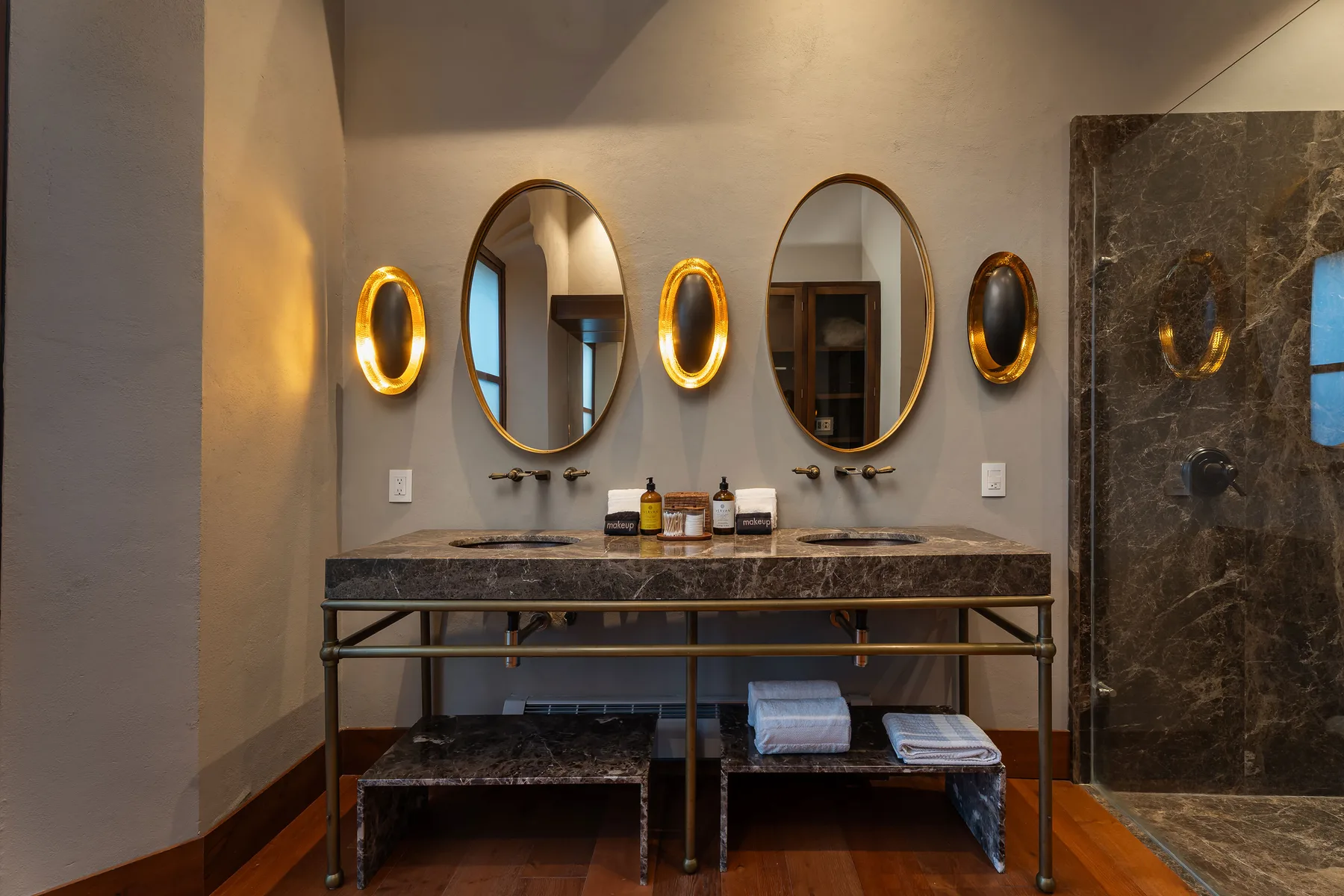A bathroom vanity with two sinks, oval mirrors, and warm wall lights.