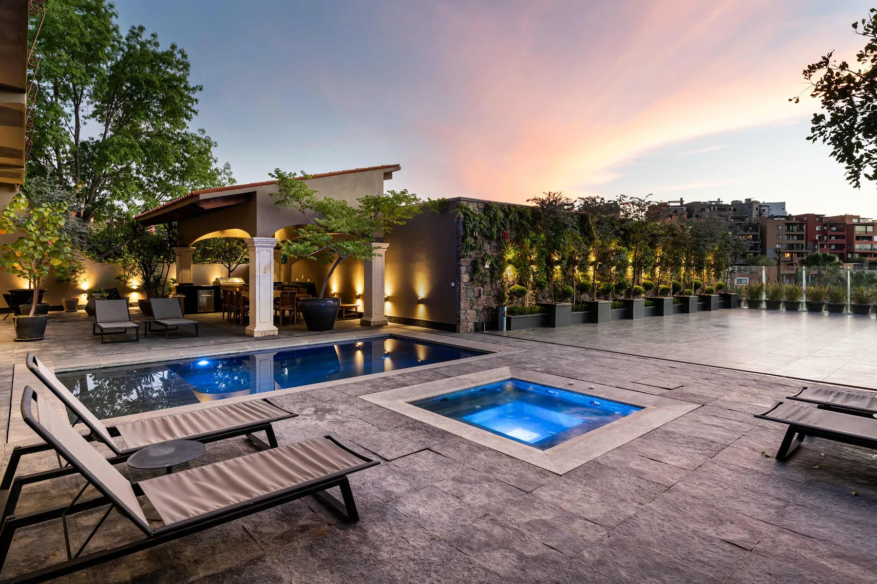 A rooftop pool and spa sit beside lounge seating beneath a colorful evening sky.