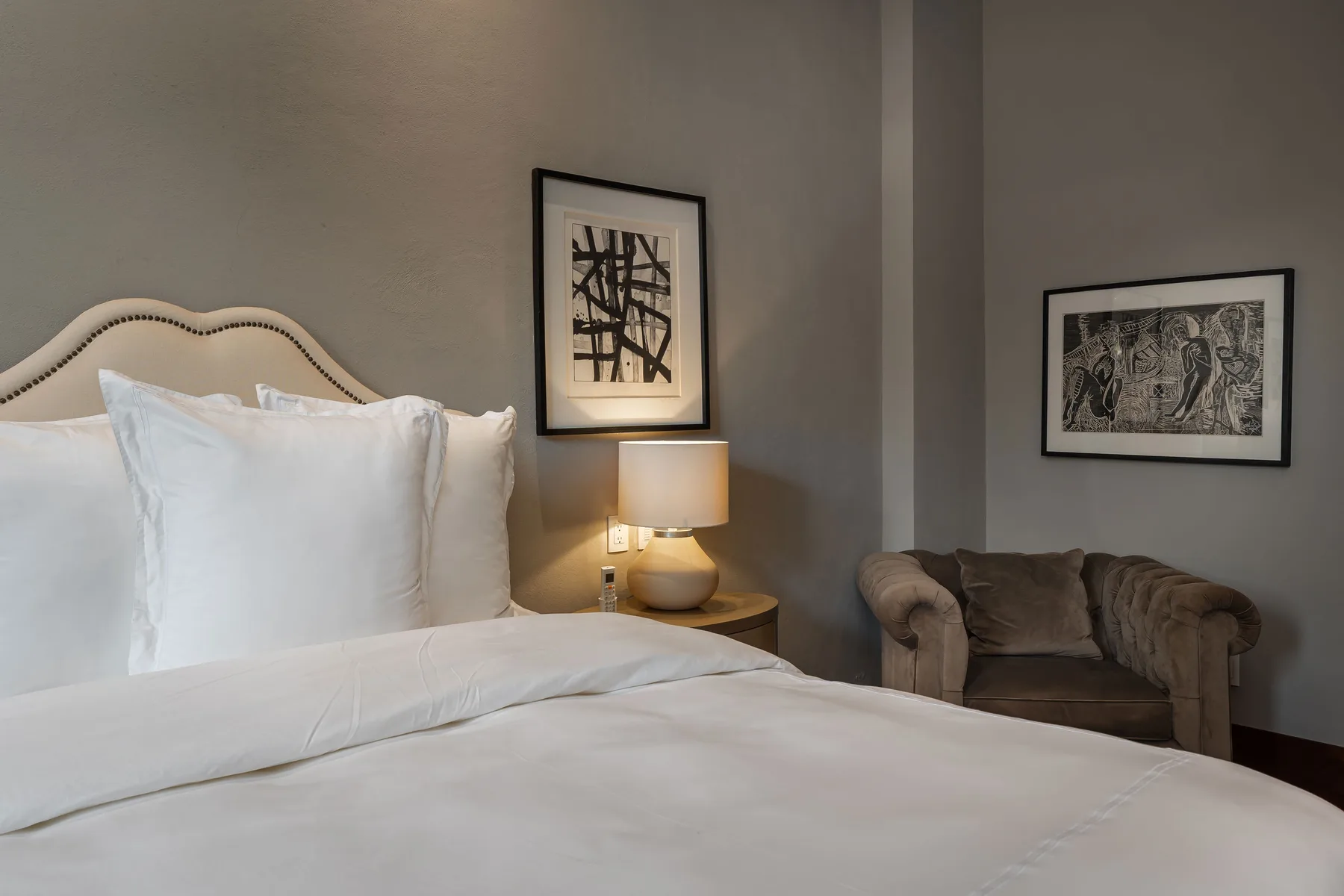 A bedroom with a neatly made bed, a bedside lamp, and an armchair.