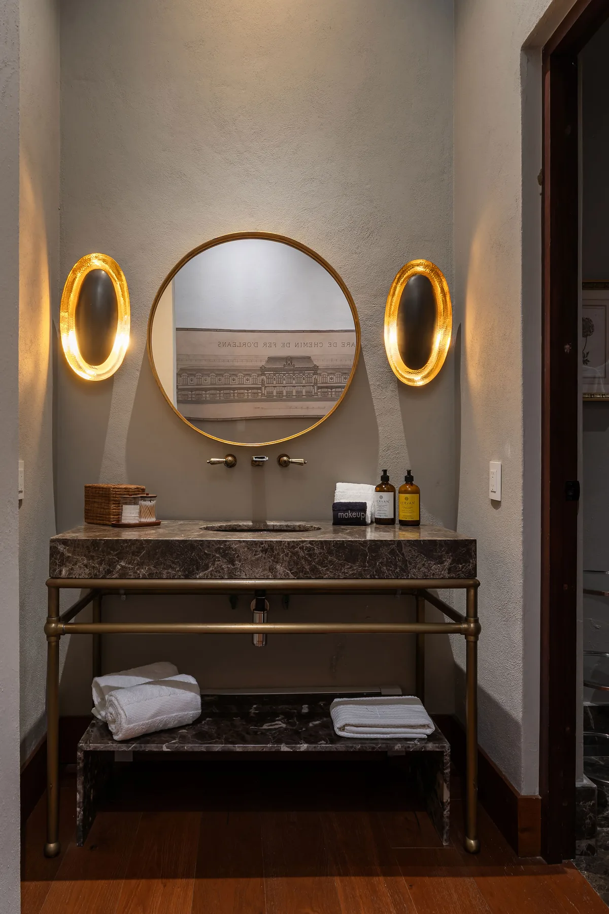A bathroom vanity with a round mirror, illuminated wall lights, and folded towels.