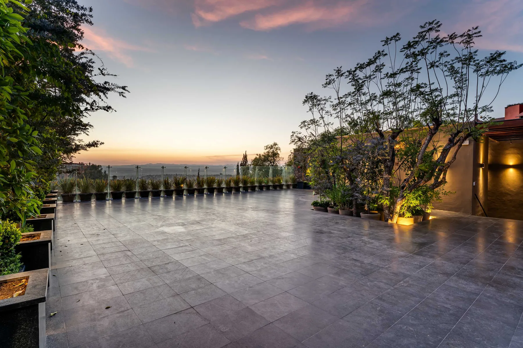 An open tiled terrace with potted plants overlooks the water at sunset.