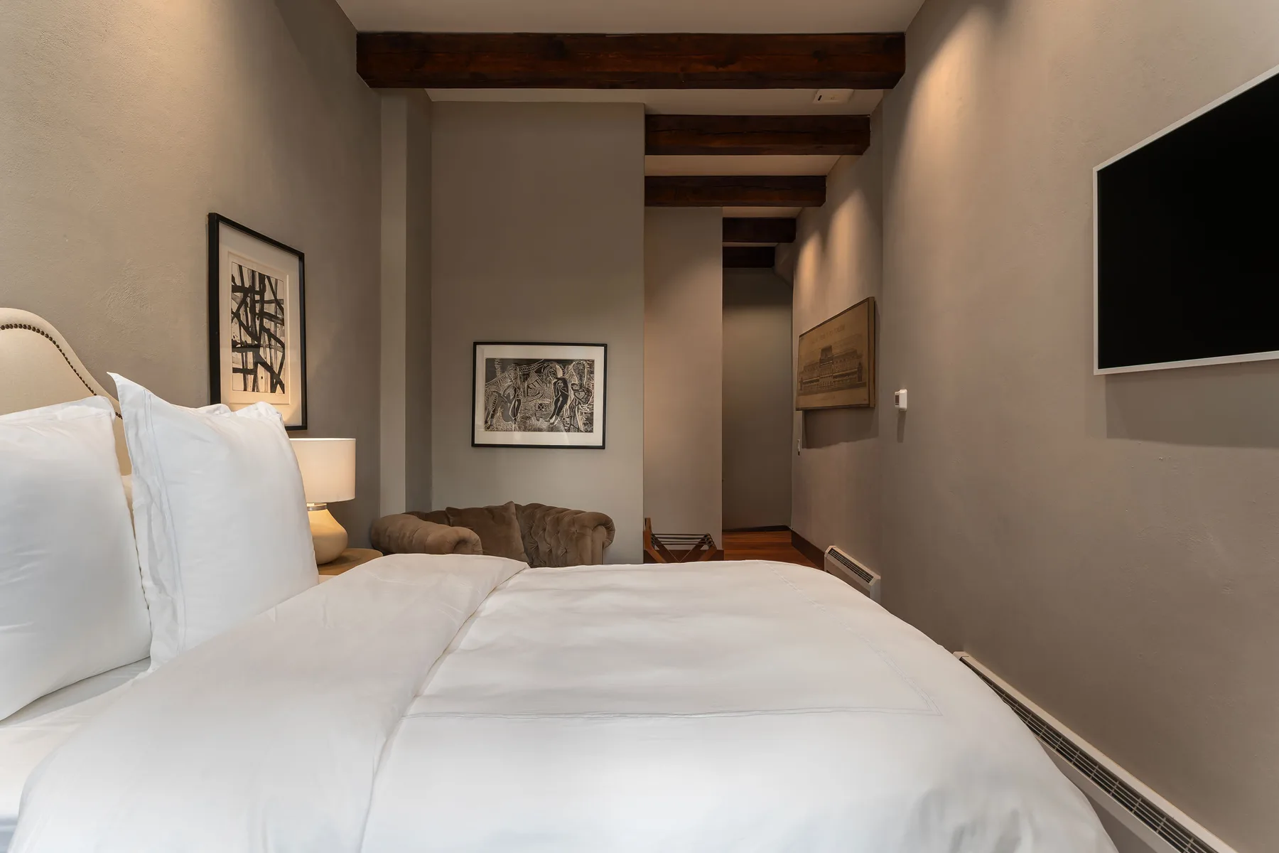 A bedroom with a large bed, framed artwork, and a wall-mounted television.