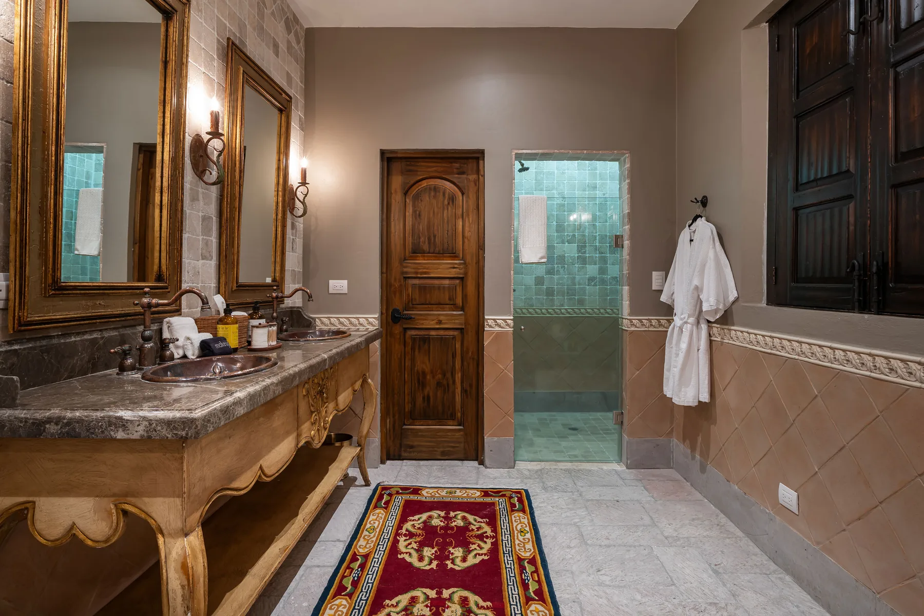 A tiled bathroom with a wooden vanity, a central door, and a glass shower.
