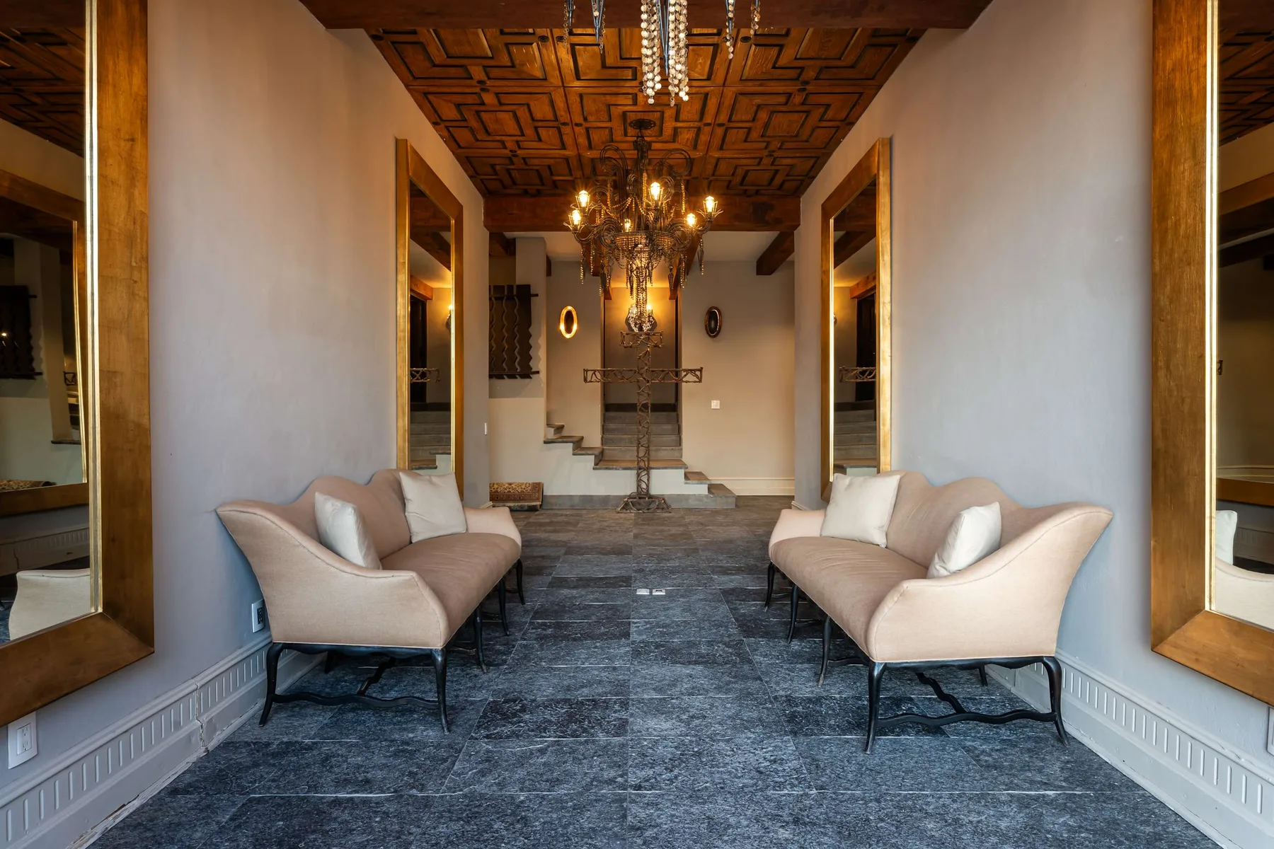 A formal sitting area with upholstered seating, chandeliers, and a patterned ceiling.