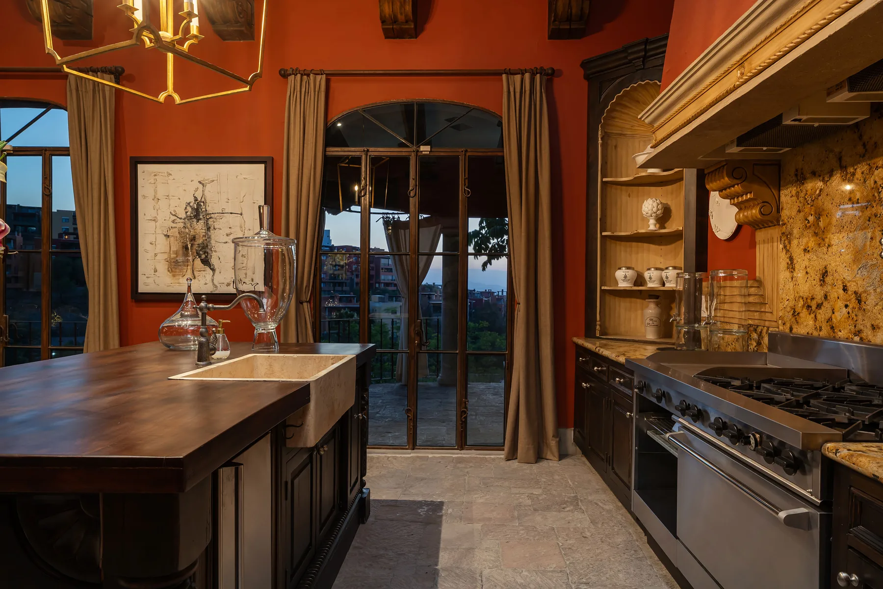 A warm-toned kitchen with a central island, tall windows, and cooking counters.