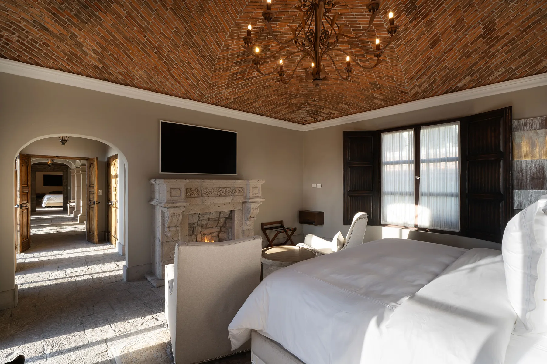 A bedroom with a large bed, fireplace, and brick vaulted ceiling.