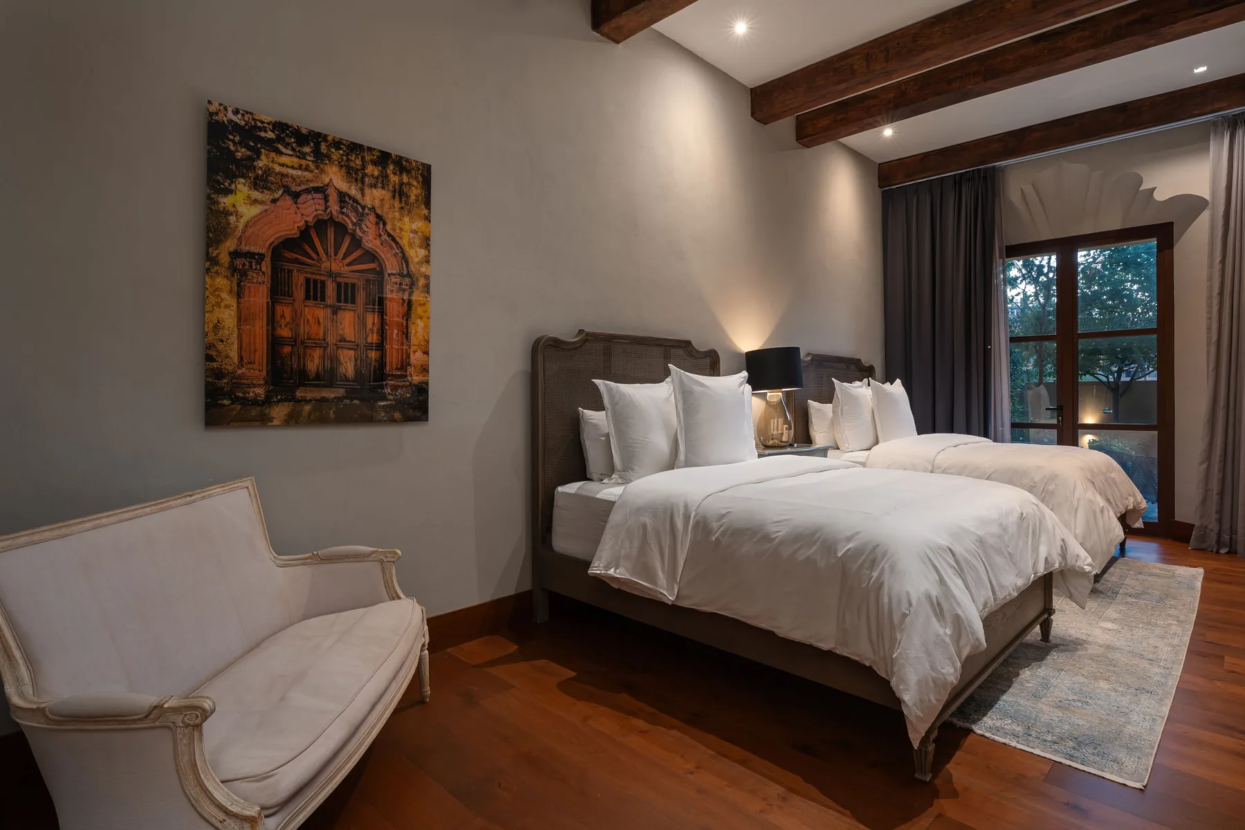 A bedroom with two beds, an upholstered chair, and exposed wooden ceiling beams.