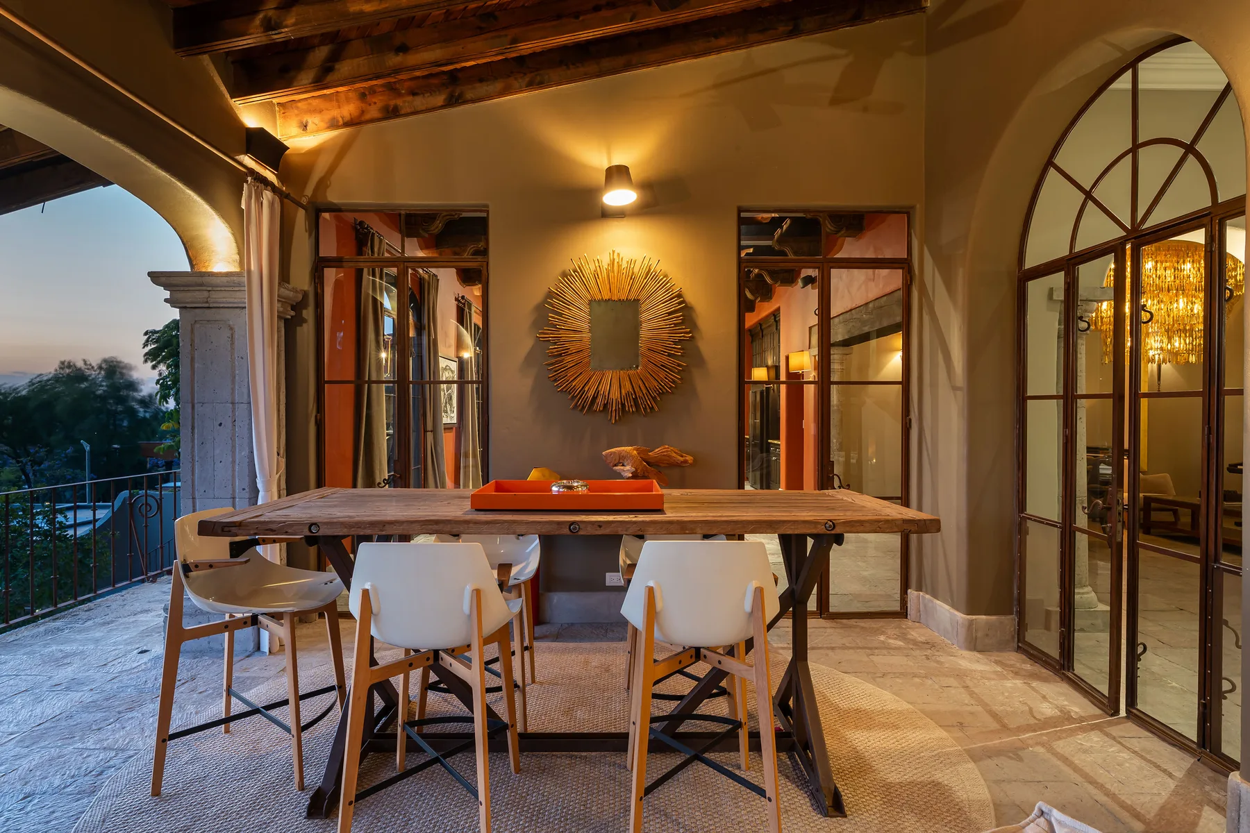 A warmly lit dining area has a long wooden table beneath exposed ceiling beams.