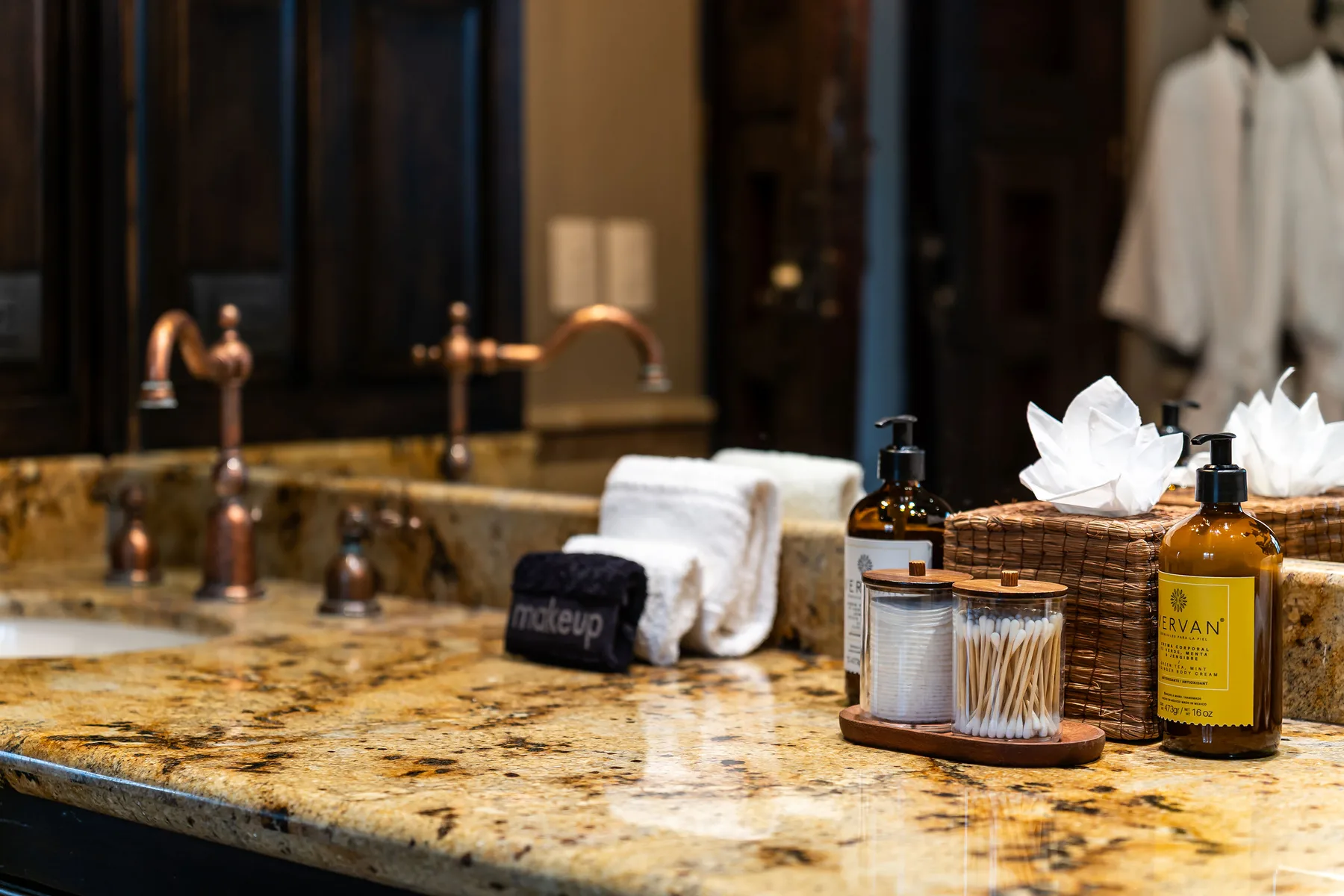 A bathroom vanity with a stone countertop, towels, and toiletries.