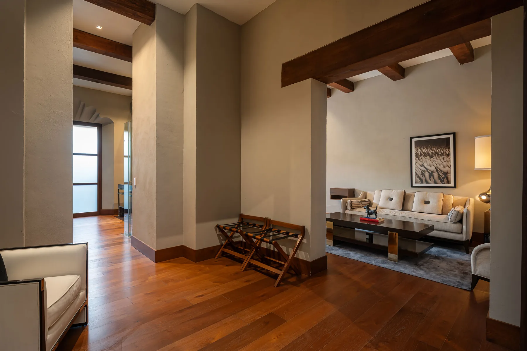 A warm-toned living room with wood flooring, exposed beams, and a seating area.