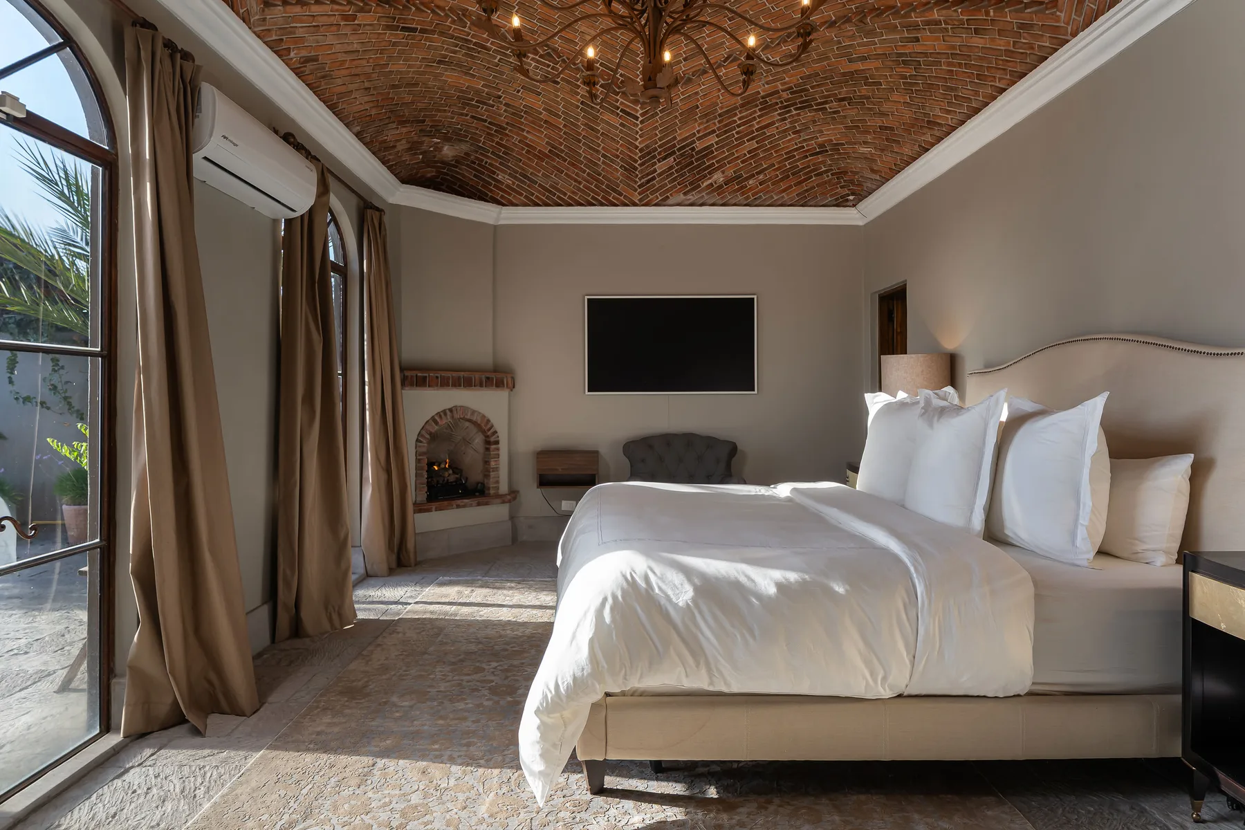 A bright bedroom with a large bed, white bedding, and tall windows.