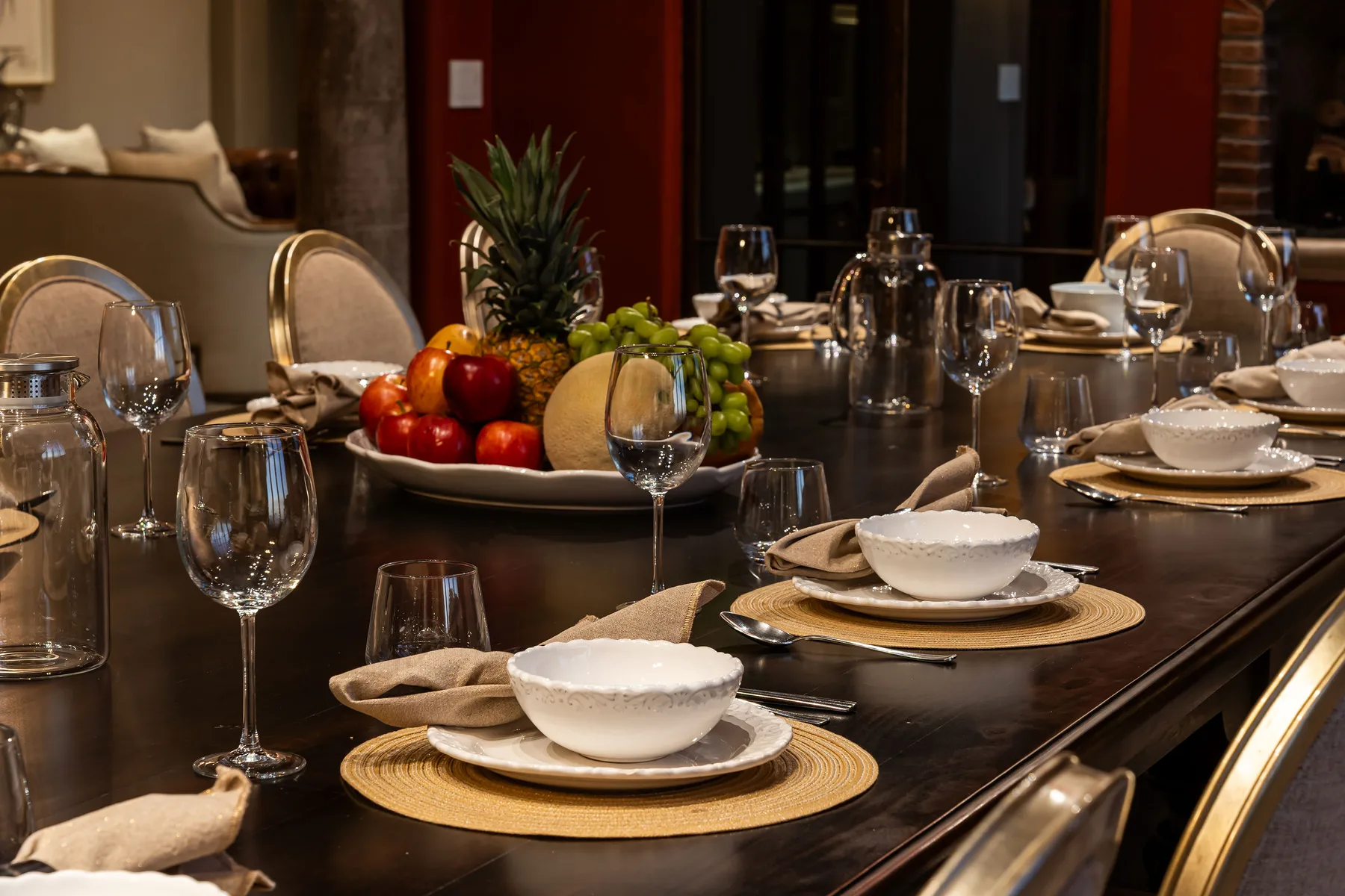 A dining table is set with dishes, glassware, and a fruit centerpiece.