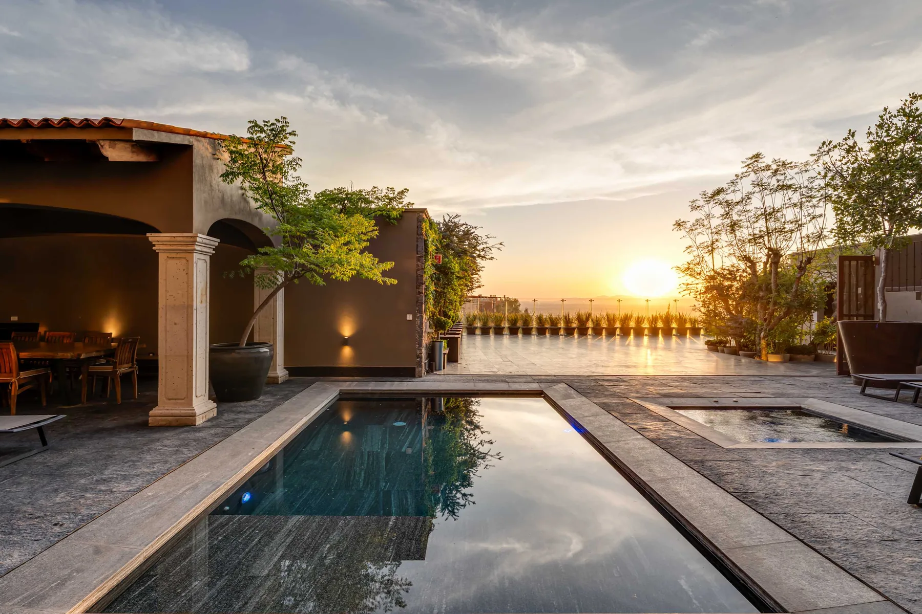 An outdoor pool and patio overlook the water at sunset.