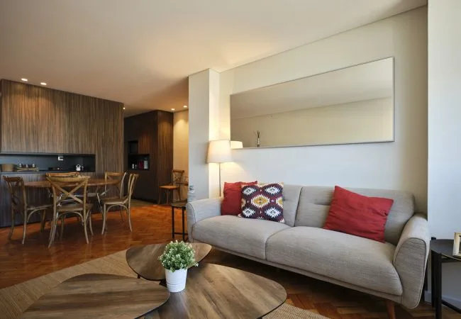 A living room with a gray sofa and a dining area behind it.