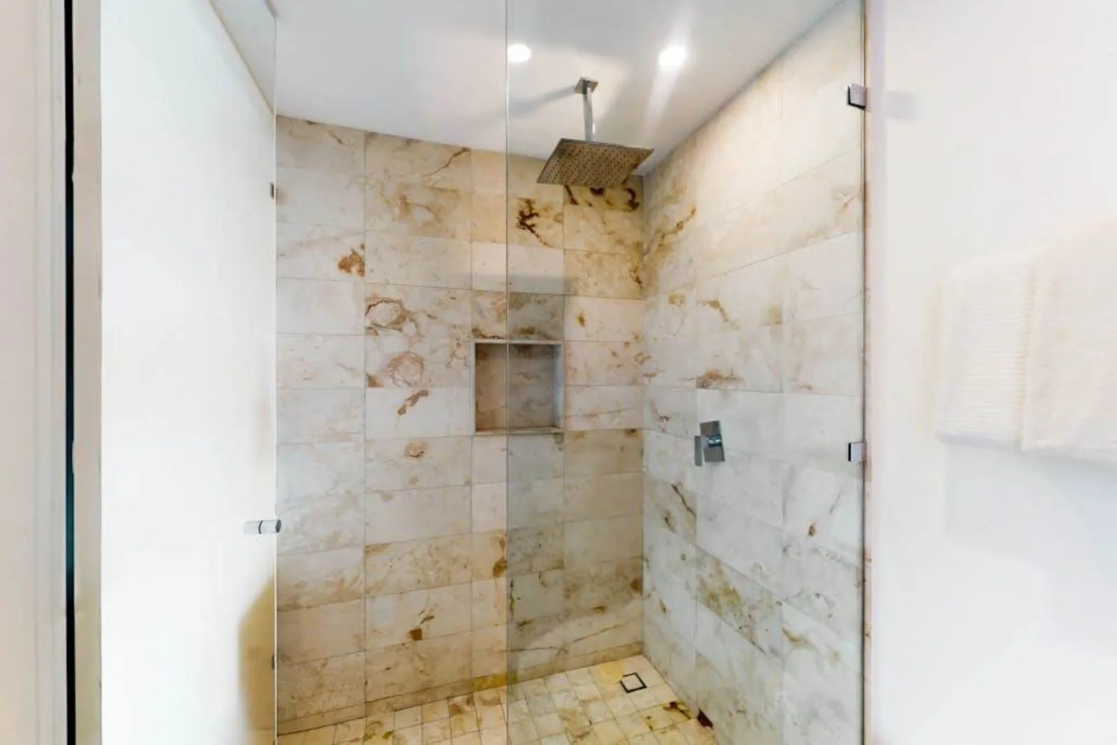 Una ducha revestida de azulejos, con un nicho en la pared y una ducha superior.