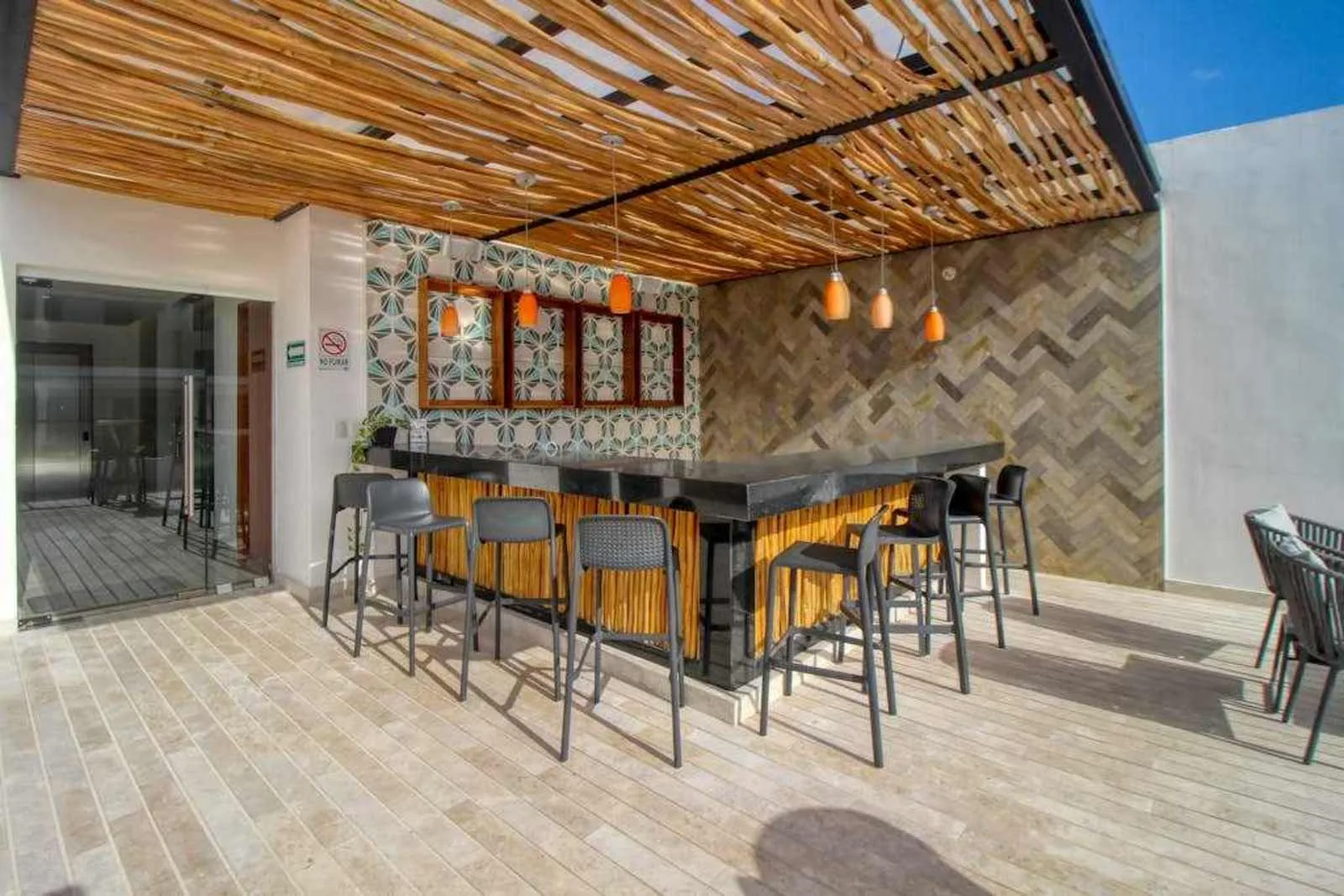 Zona común: Una barra con taburetes está bajo un toldo de listones en una zona de estar al aire libre.