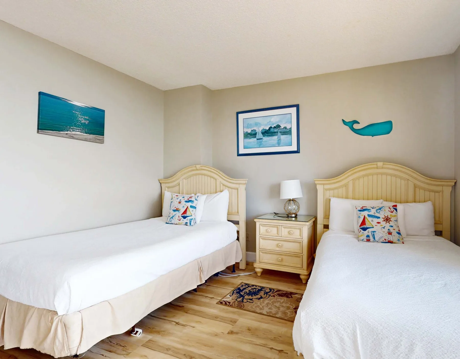 A bedroom with two beds, a nightstand, and coastal artwork on the walls.