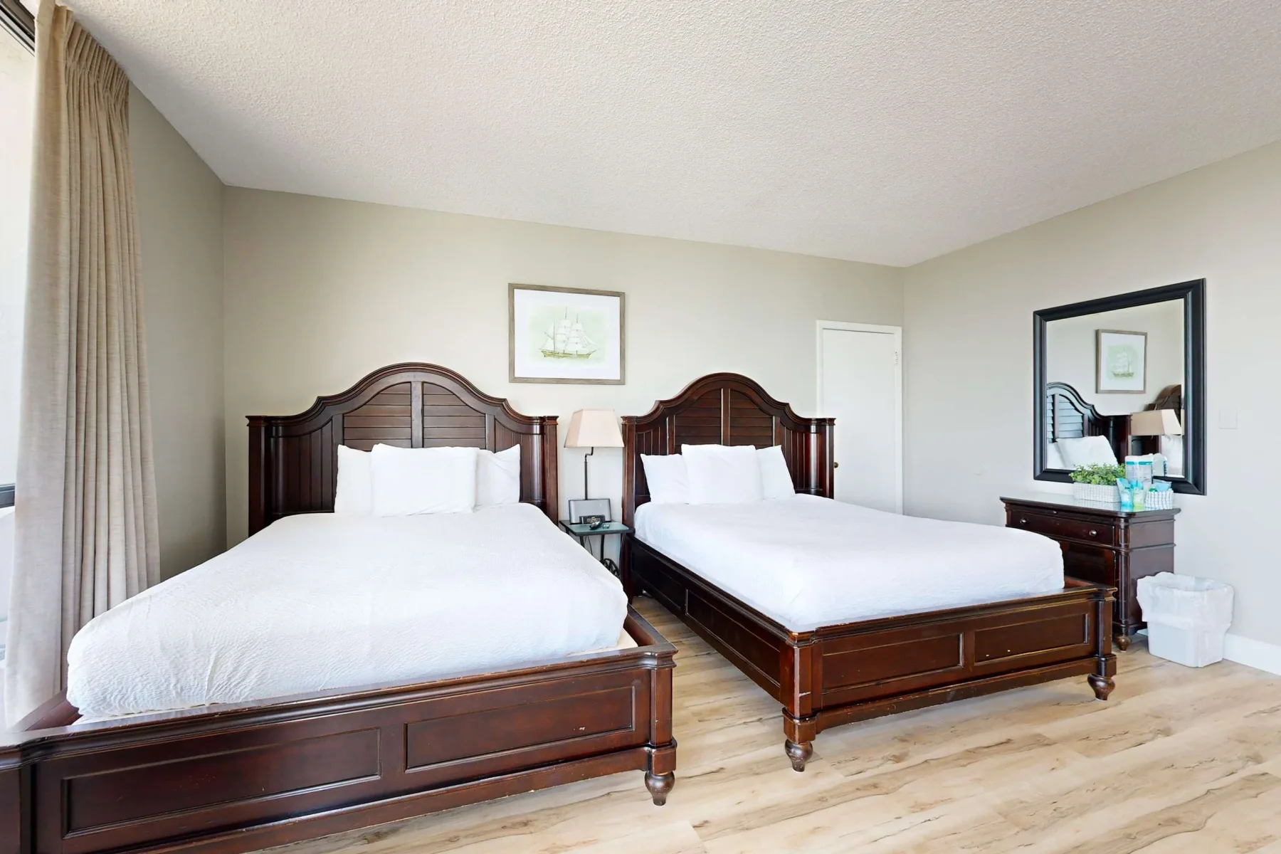 A bedroom with two beds and a dresser beneath a wall mirror.