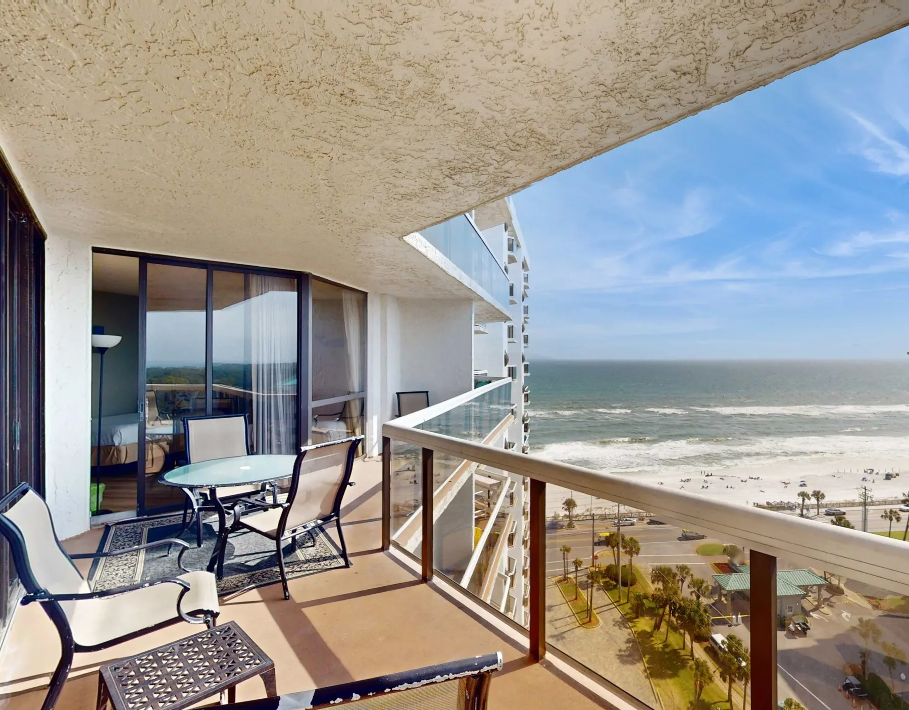 A balcony overlooking the beach and ocean, with seating beside the glass railing.