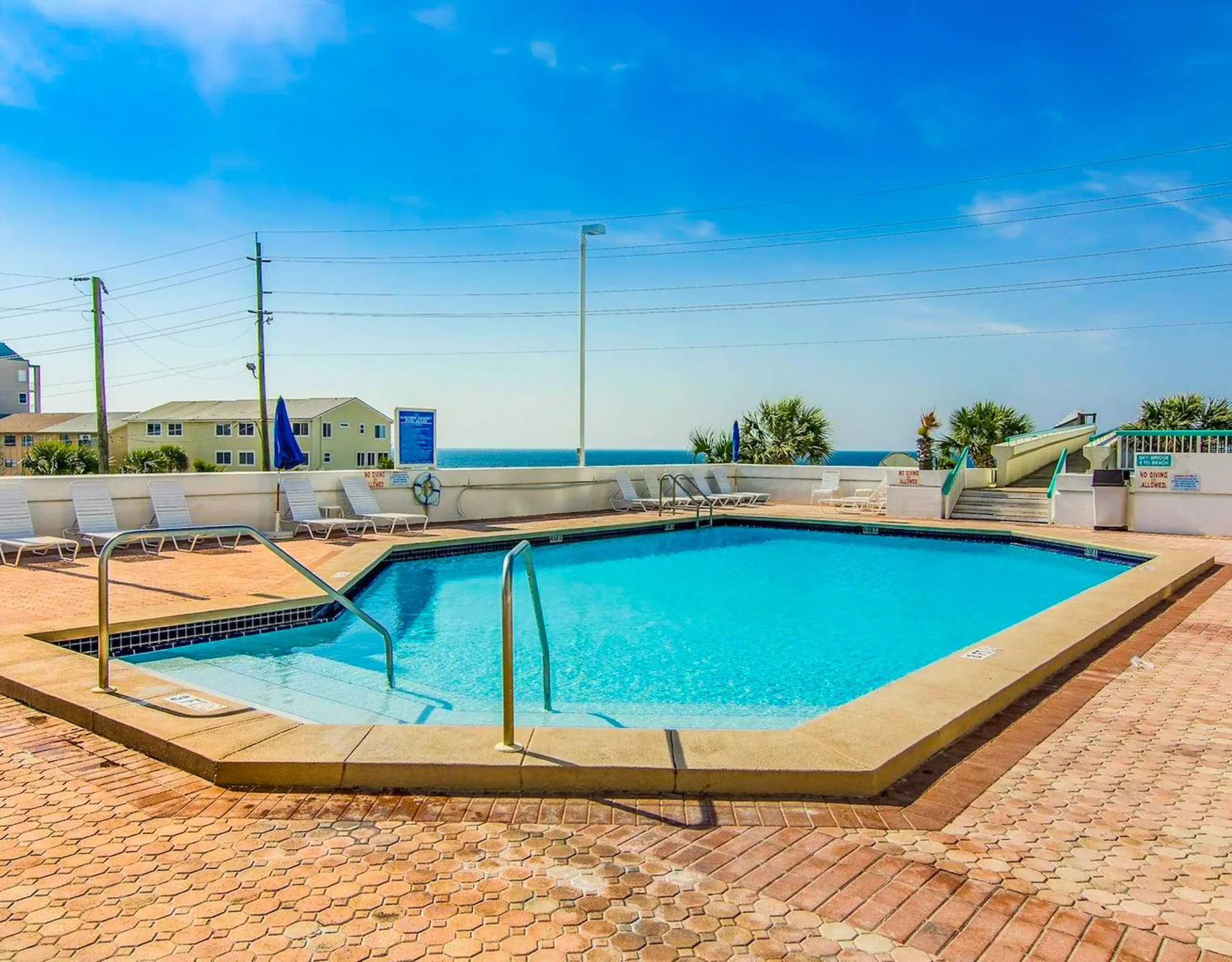 Shared amenity: An outdoor swimming pool sits on a sunny paved deck beside the sea.