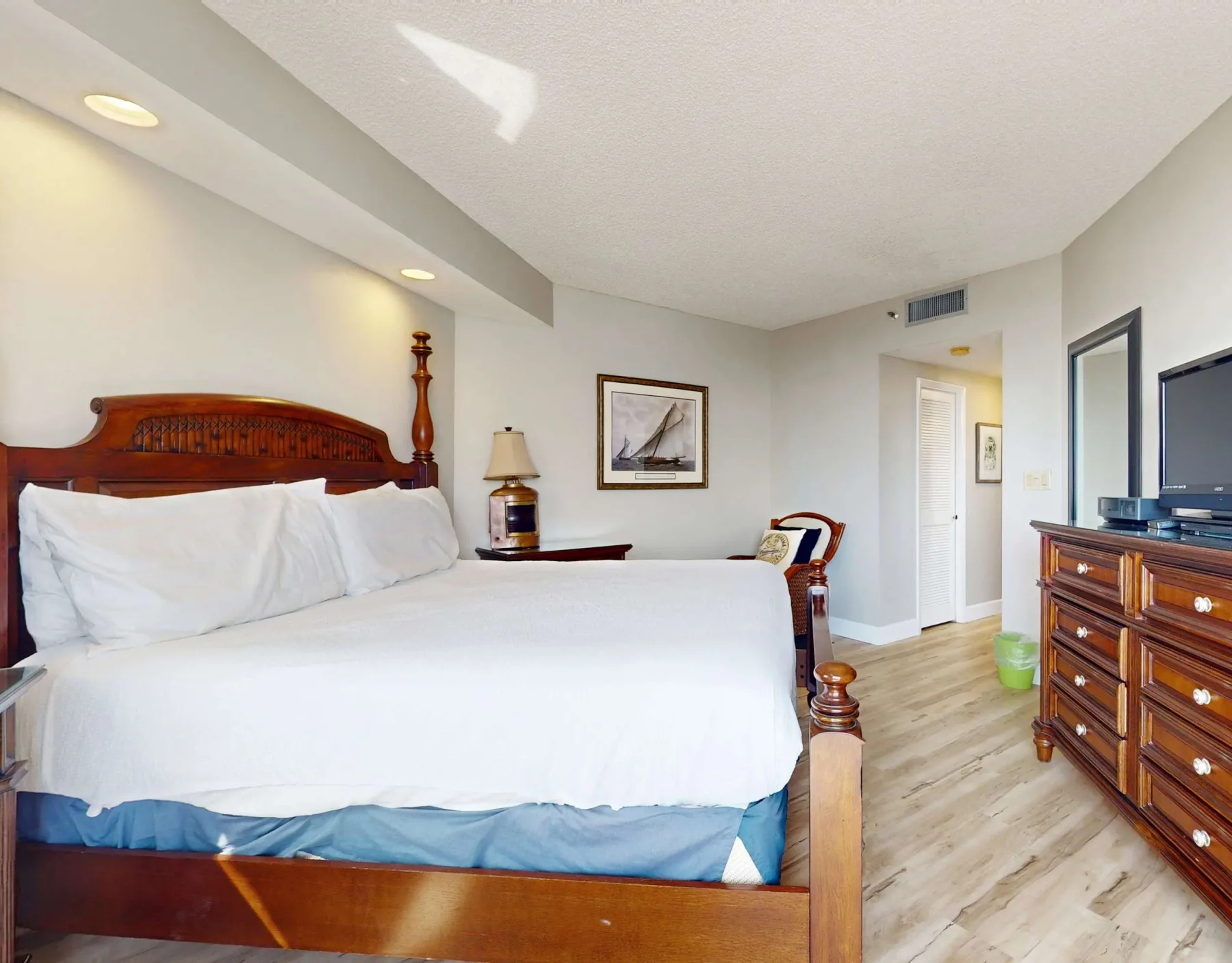 A bedroom with a large bed, white bedding, and a wooden dresser.