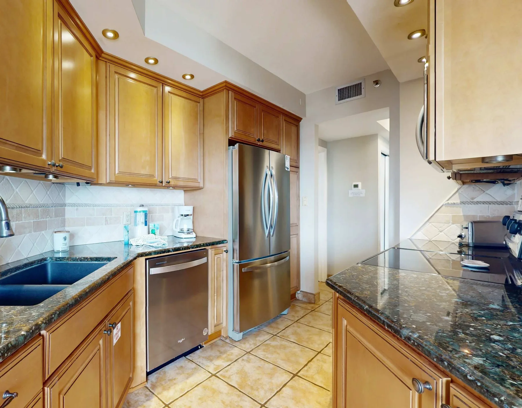 A kitchen with wooden cabinets, stone counters, and stainless steel appliances.