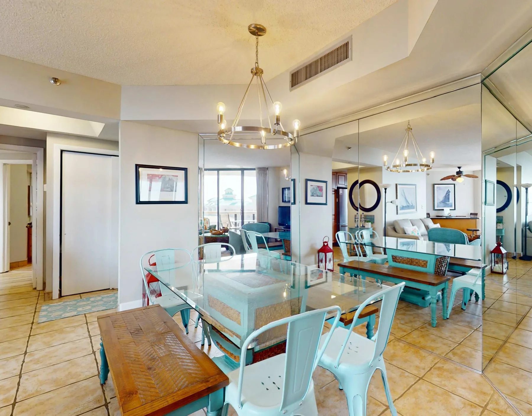 A bright dining area with a glass table, pale chairs, and a large wall mirror.