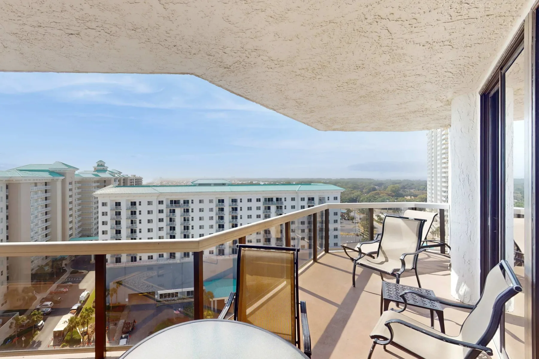 A balcony with seating overlooks nearby buildings and a swimming pool.