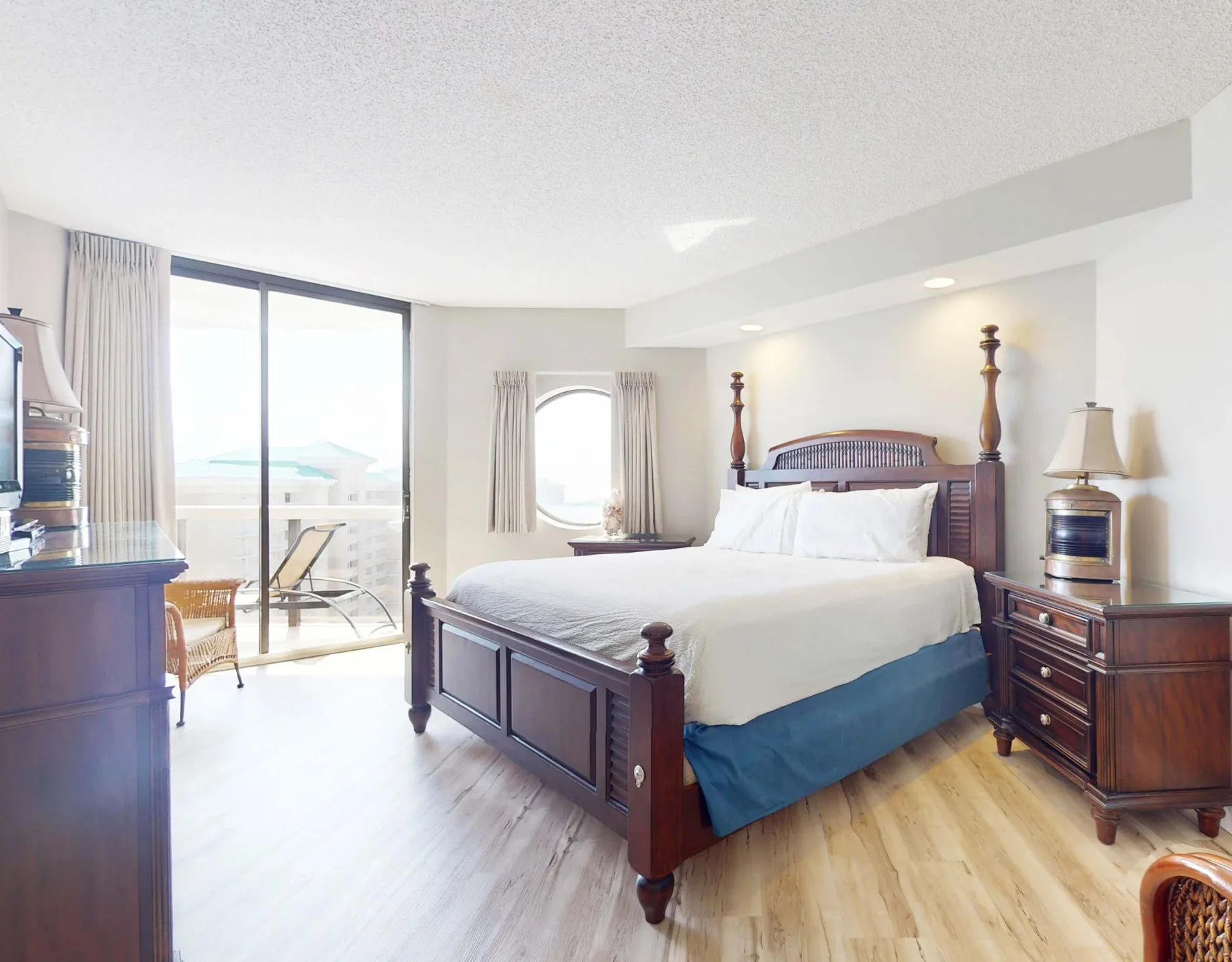 A bright bedroom with a large bed and sliding glass doors opening to a balcony.
