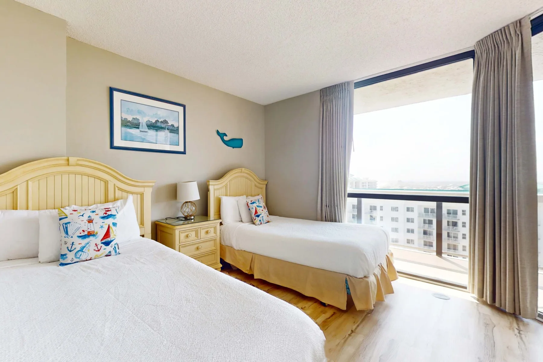 A bright bedroom with two beds beside a large window.