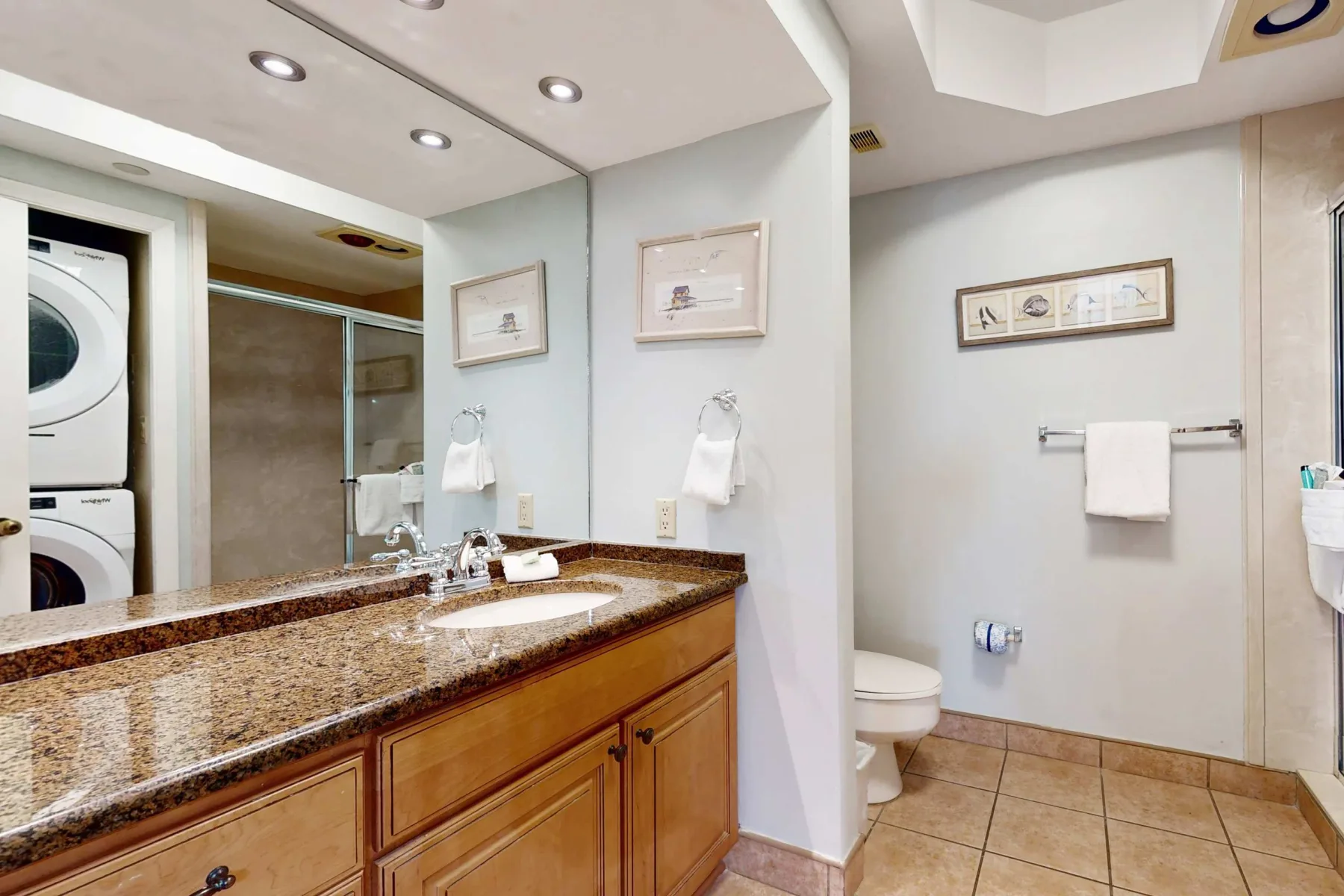 A bathroom vanity and mirror overlook a toilet and tiled floor.