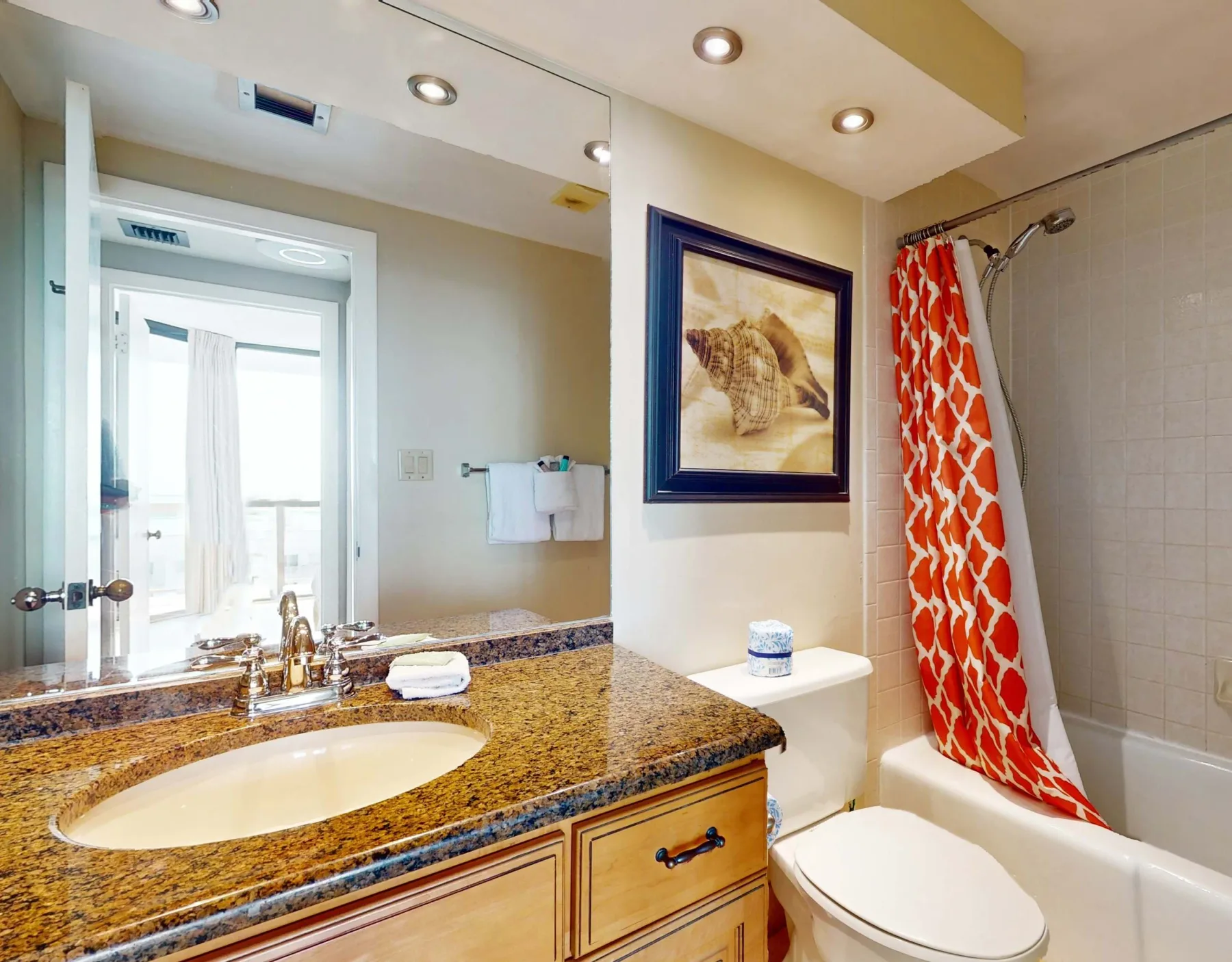 A bathroom with a sink vanity, mirror, toilet, and shower with a patterned curtain.