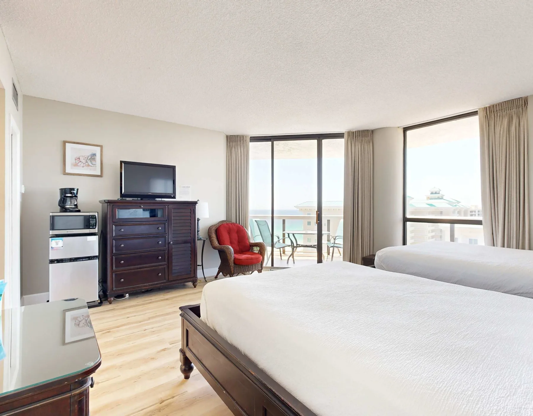A bright bedroom with a large bed, dark dresser, and windows opening onto a balcony.