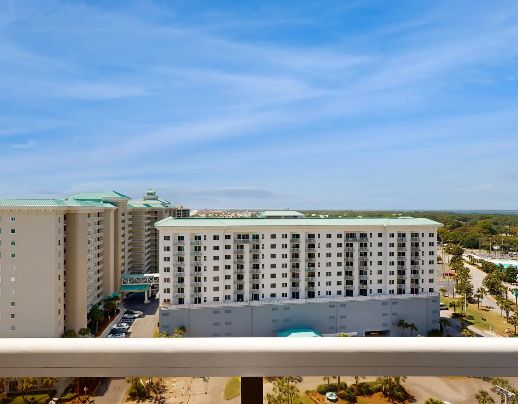 Apartment buildings stand beneath a broad blue sky, viewed from behind a balcony railing.