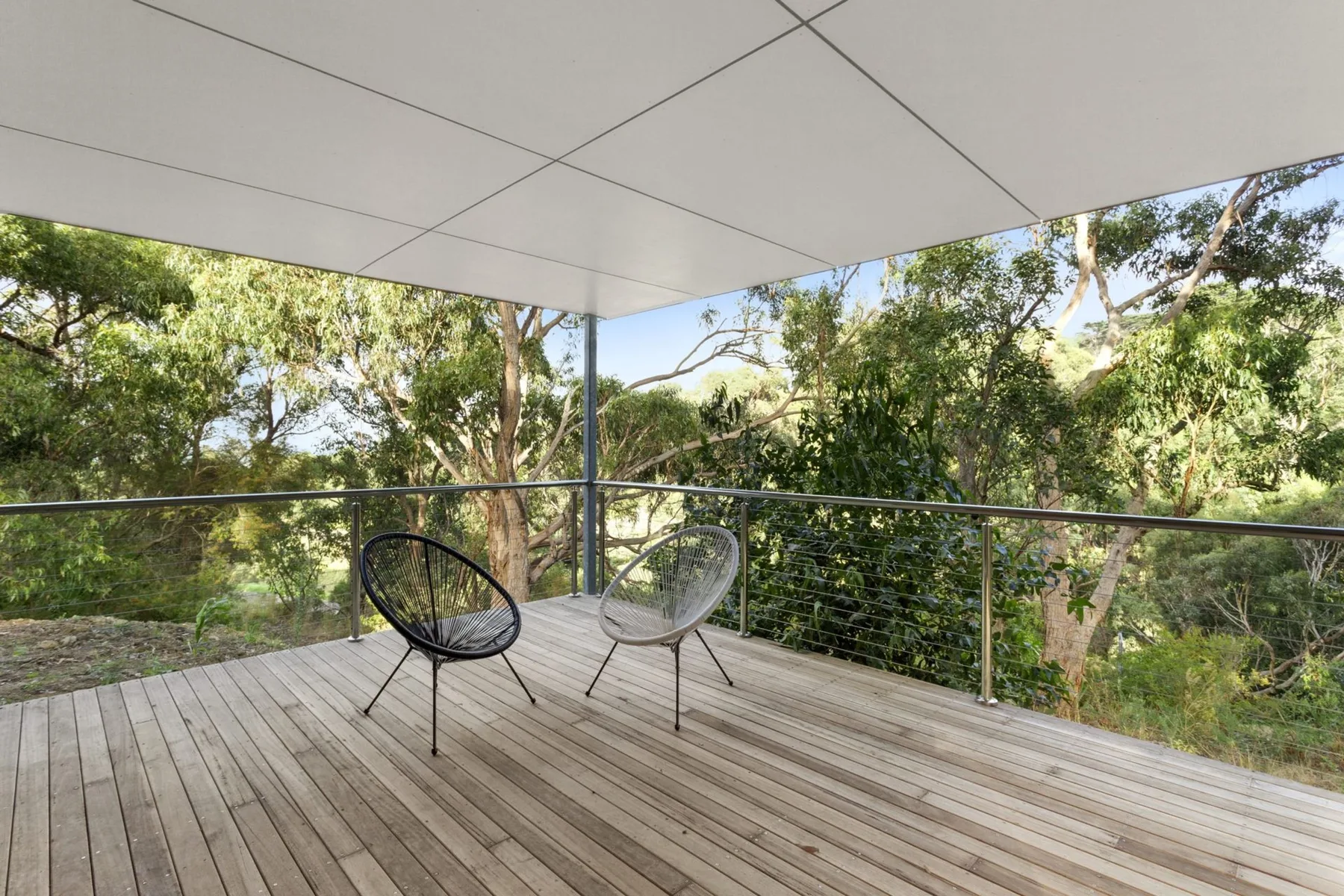 A covered outdoor deck with two chairs overlooking leafy trees.