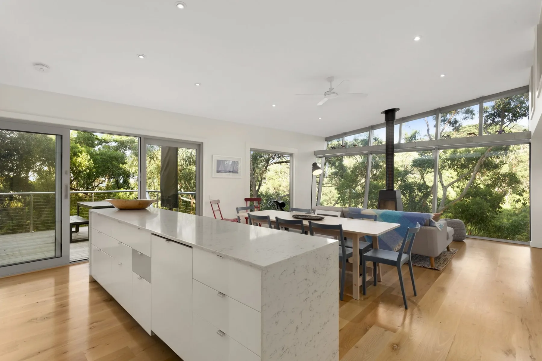 An open-plan kitchen and dining area with a large island and windows overlooking trees.